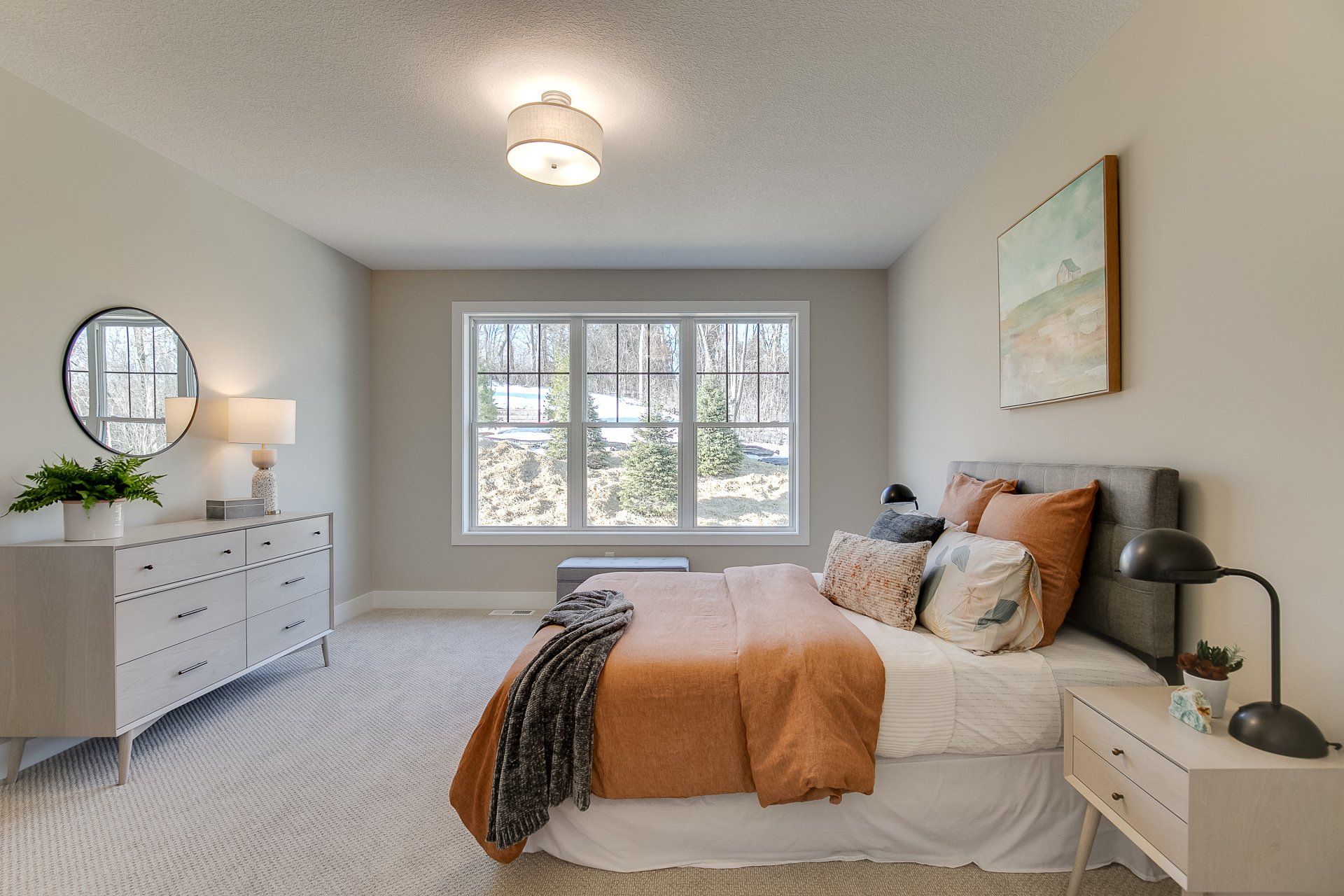 A bedroom with a bed, dresser, nightstand, mirror, and window.