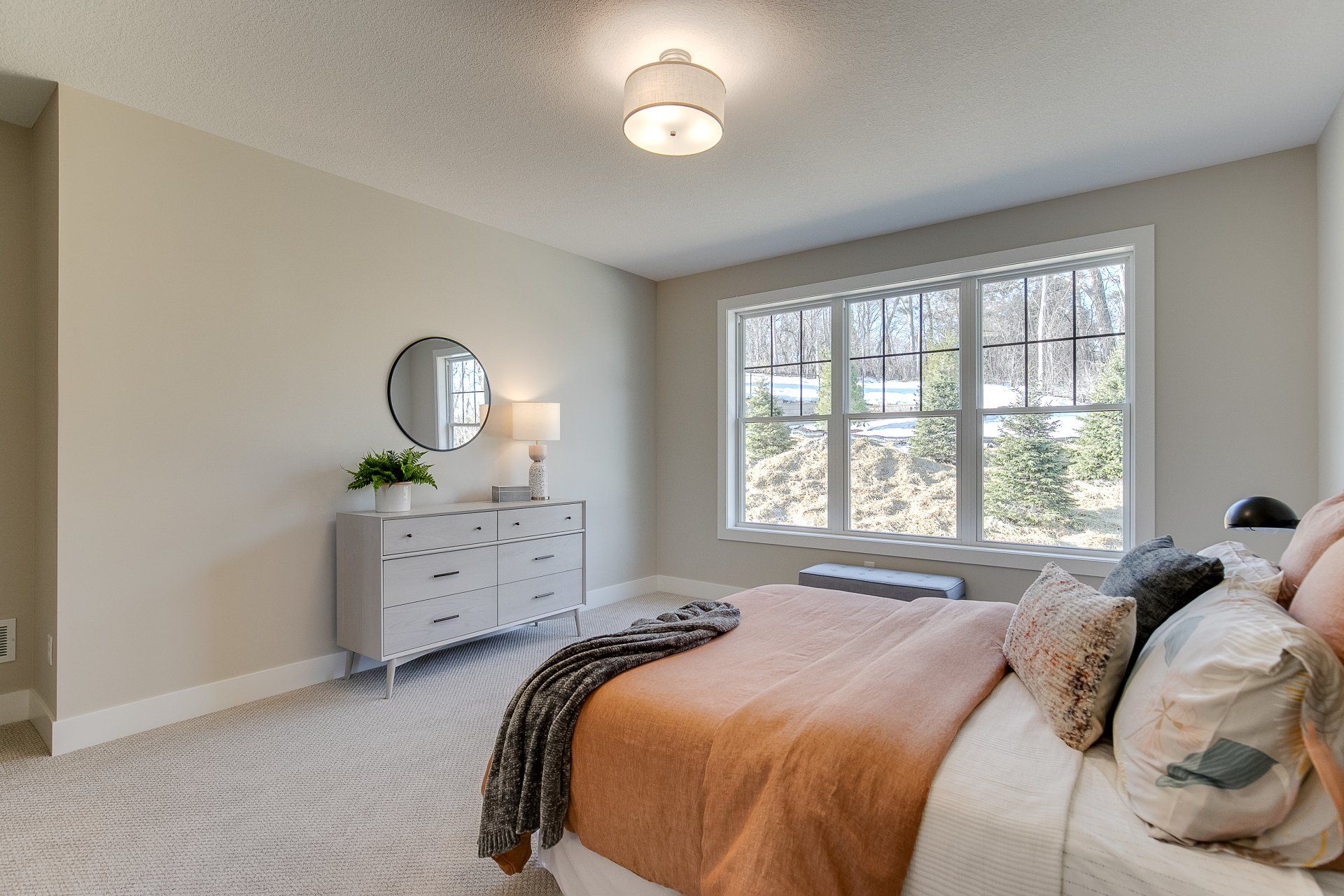 A bedroom with a bed, dresser, mirror, and two windows.
