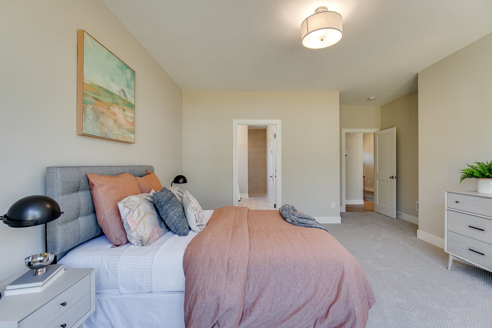 A bedroom with a bed, nightstand, dresser, and painting on the wall.