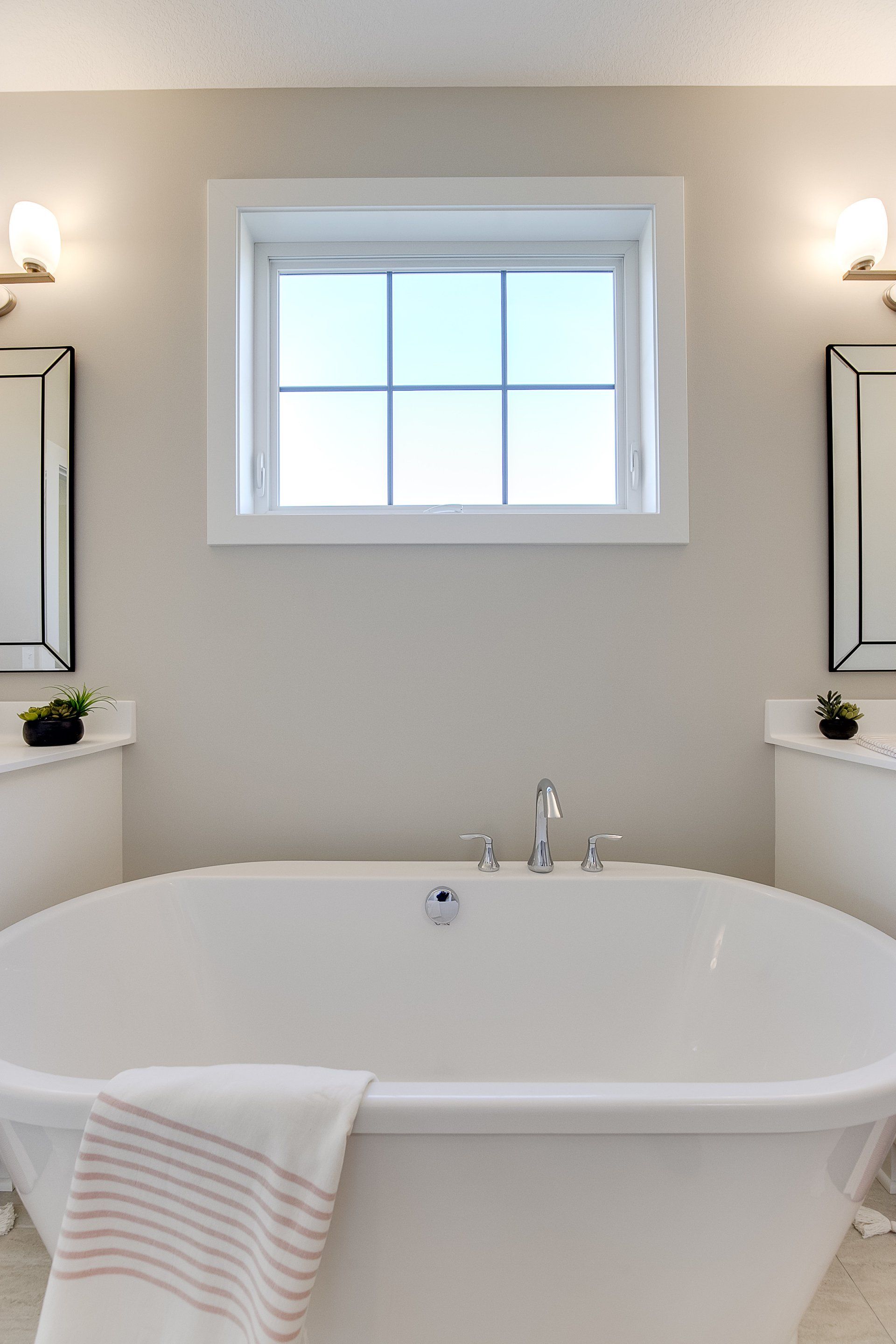 A bathroom with a tub and two mirrors and a window.