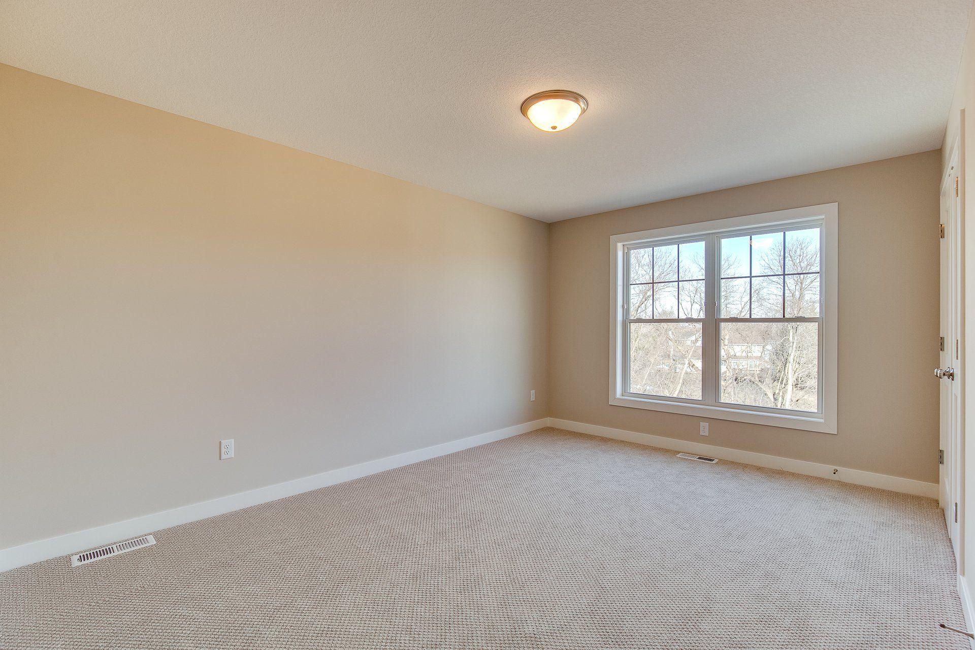 An empty bedroom with a carpeted floor and two windows.