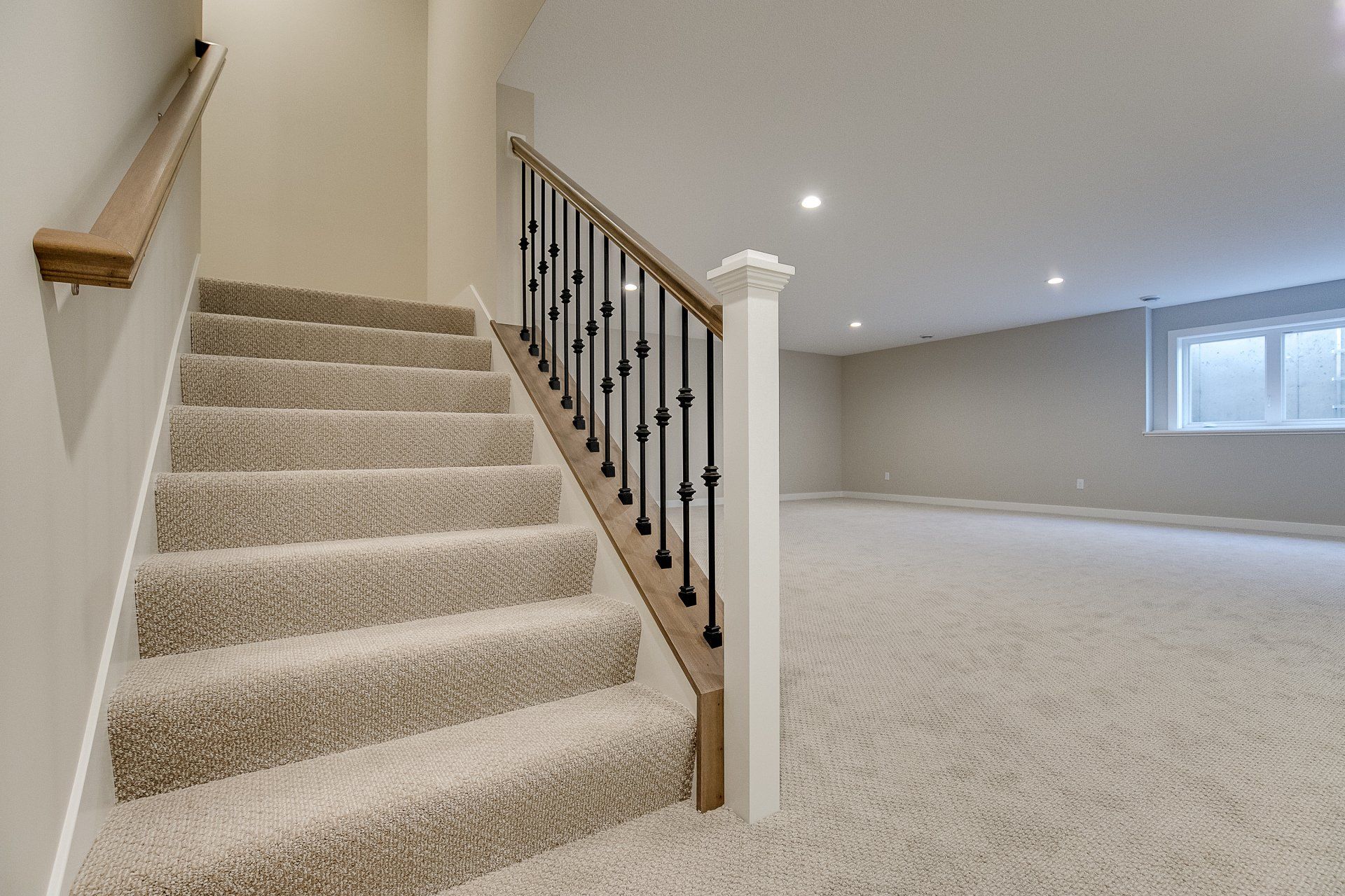 An empty basement with carpeted stairs and a railing.