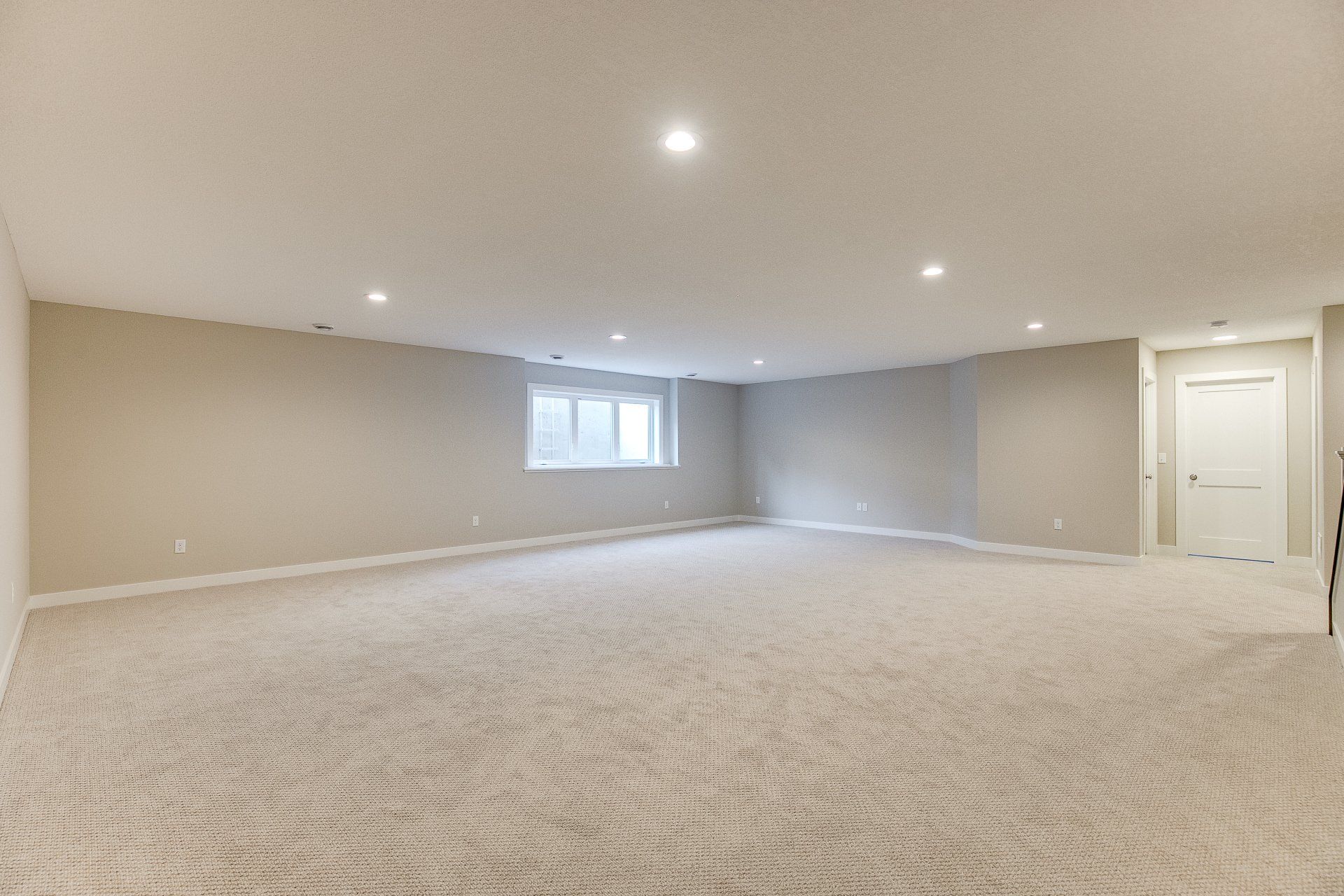An empty basement with a carpeted floor and a window.