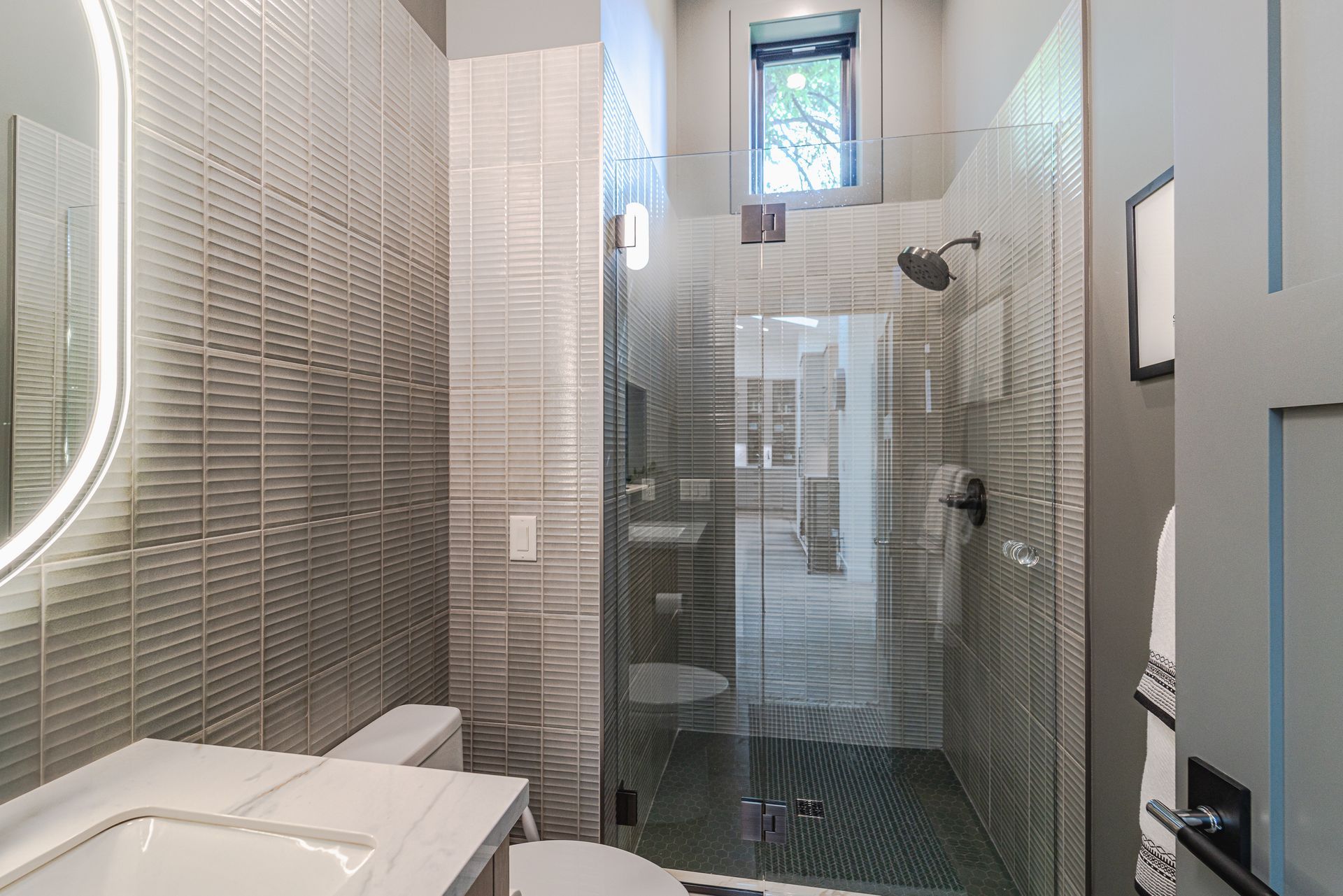 A bathroom with a walk-in shower, sink, toilet, and mirror.