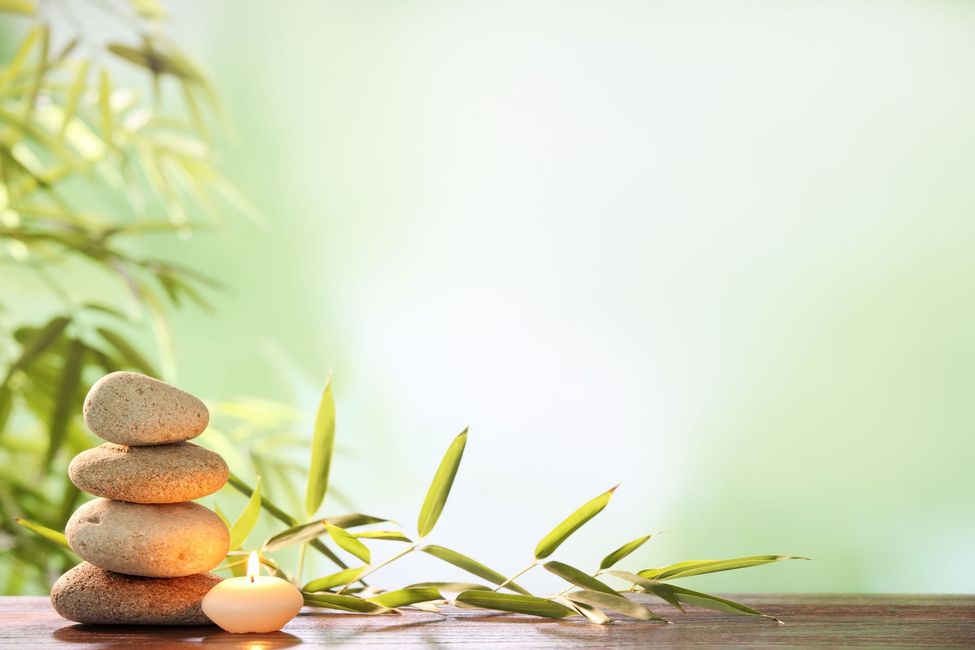 Stacked stones and bamboo sprigs with a lit tealight on a wooden surface, against a soft green background