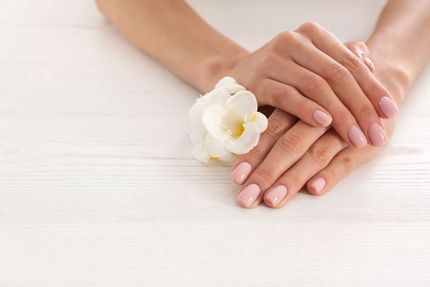 Hands with pale pink nails resting on a white surface beside a white flower