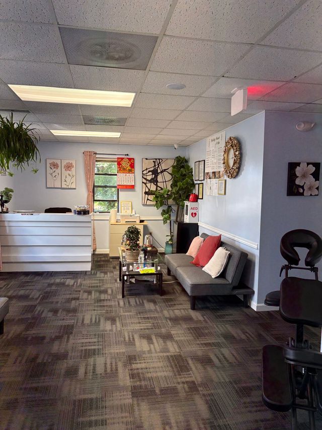 Empty office lobby with a reception desk, gray couch, potted plants, and carpeted floor.