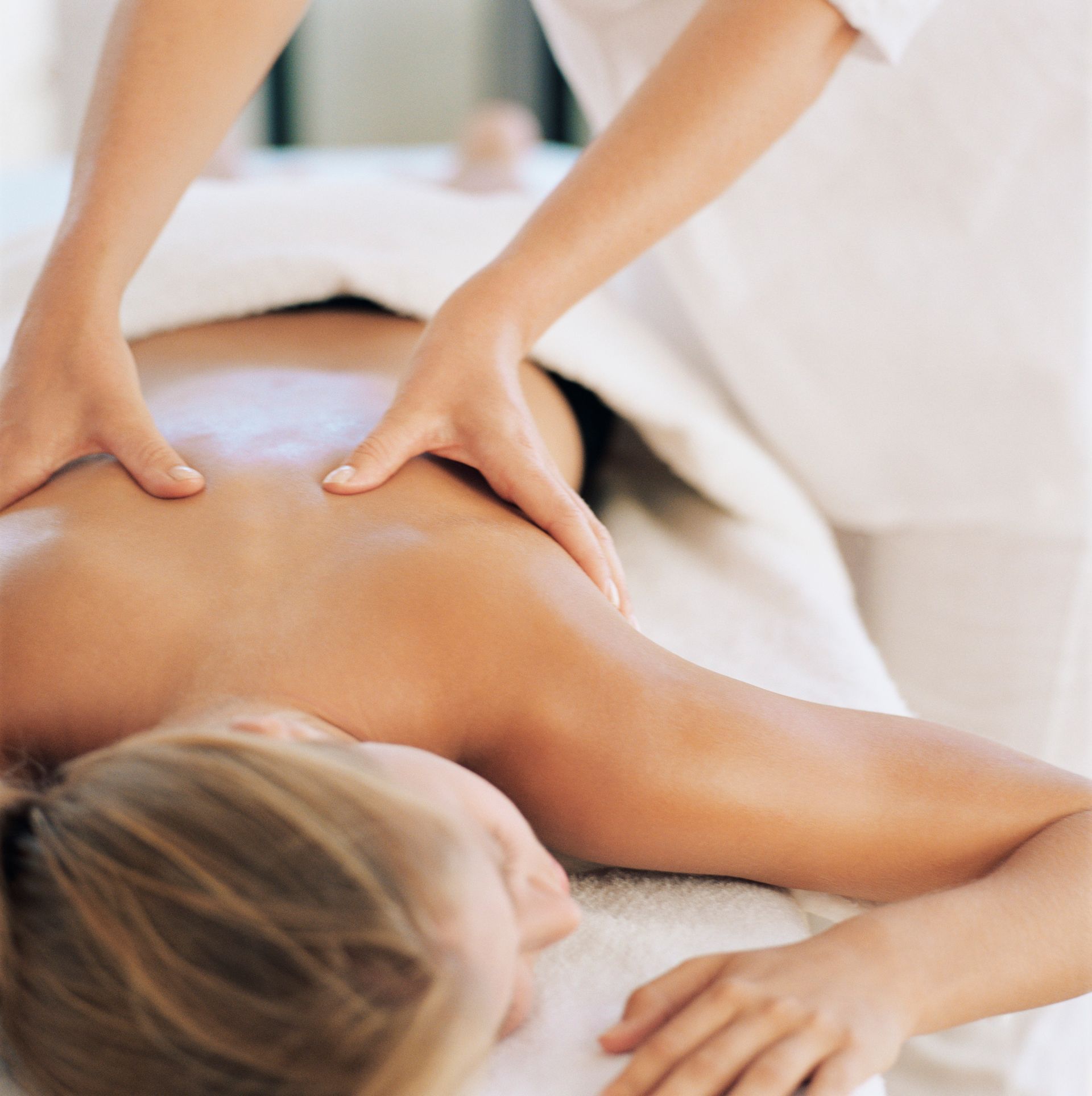 Hands giving a back massage to a person lying face down on a spa table