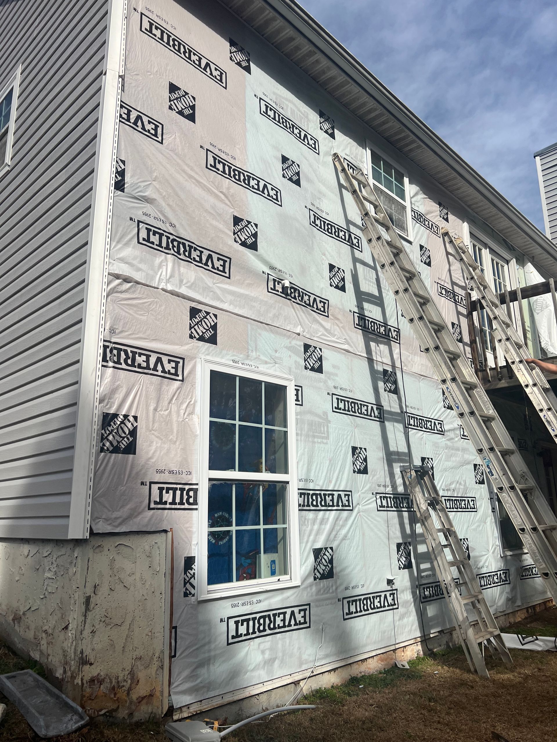 House exterior under renovation; white siding, wrap, ladder, window.