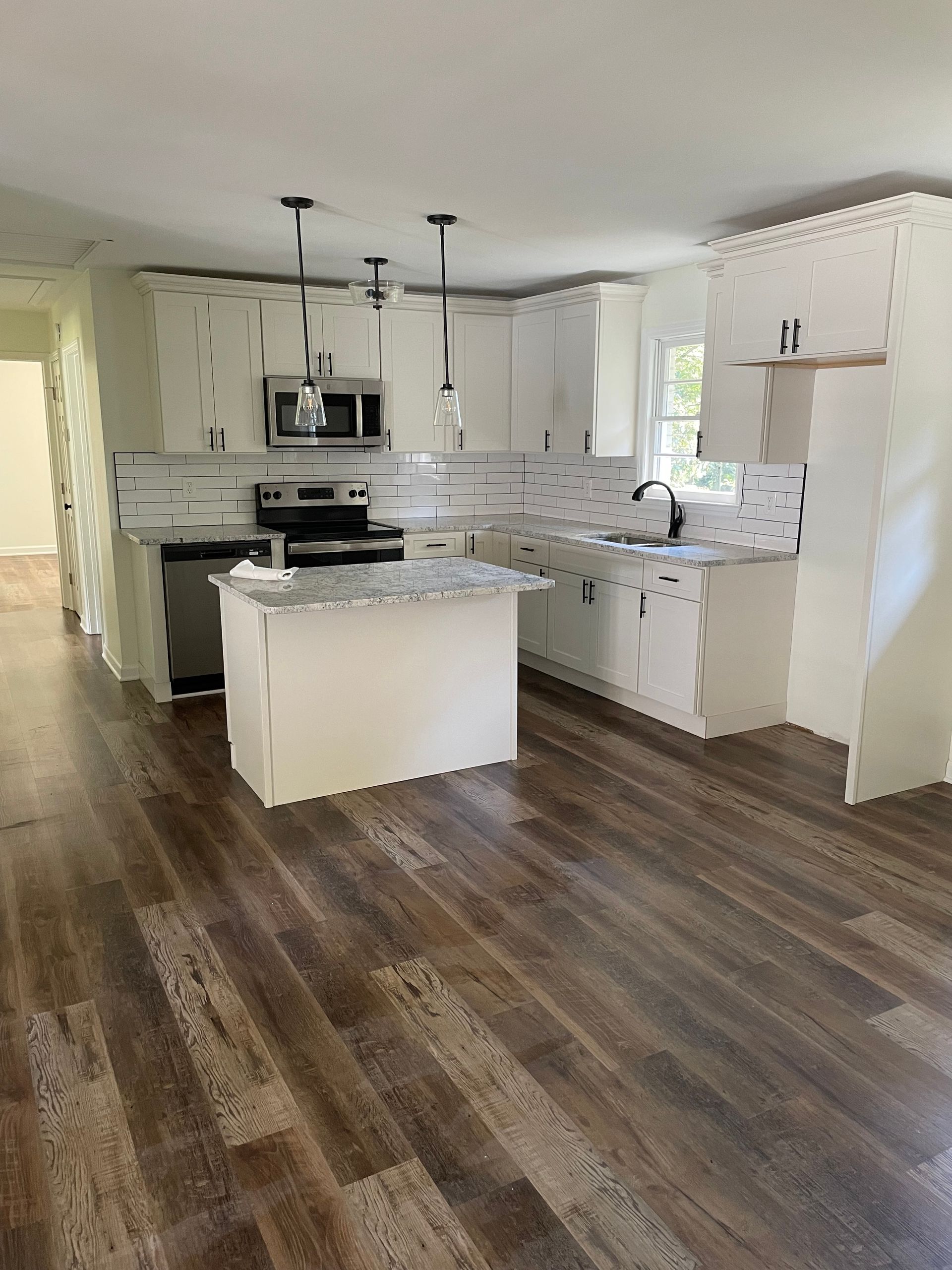 Bright, modern kitchen with white cabinets, gray countertops, and wood-look flooring. Island in the center.