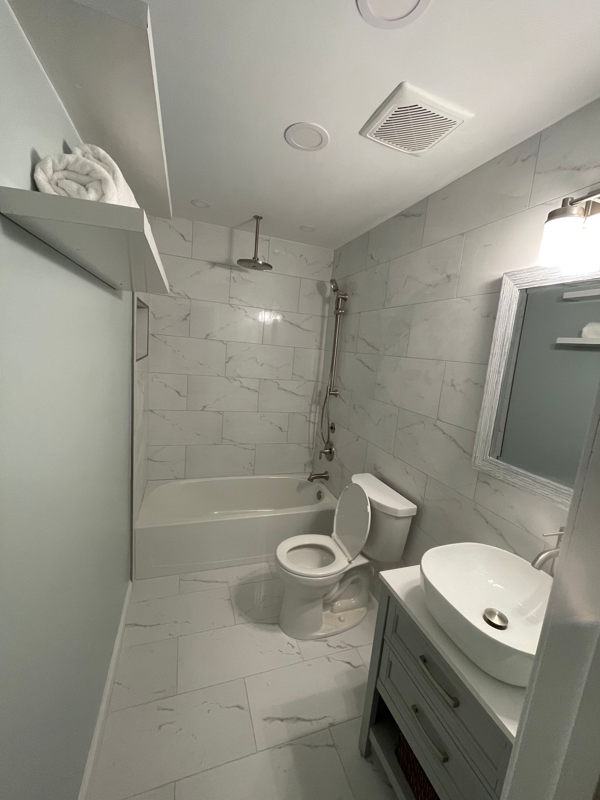 A modern bathroom with white marble walls, a toilet, sink, bathtub, and shower.