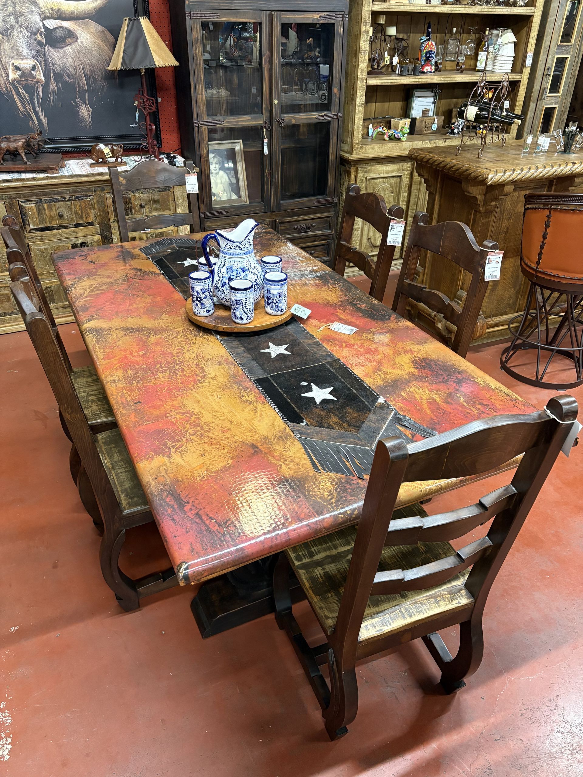 A dining table set for a meal, featuring colorful pottery, surrounded by ornate wooden chairs in a shop setting.