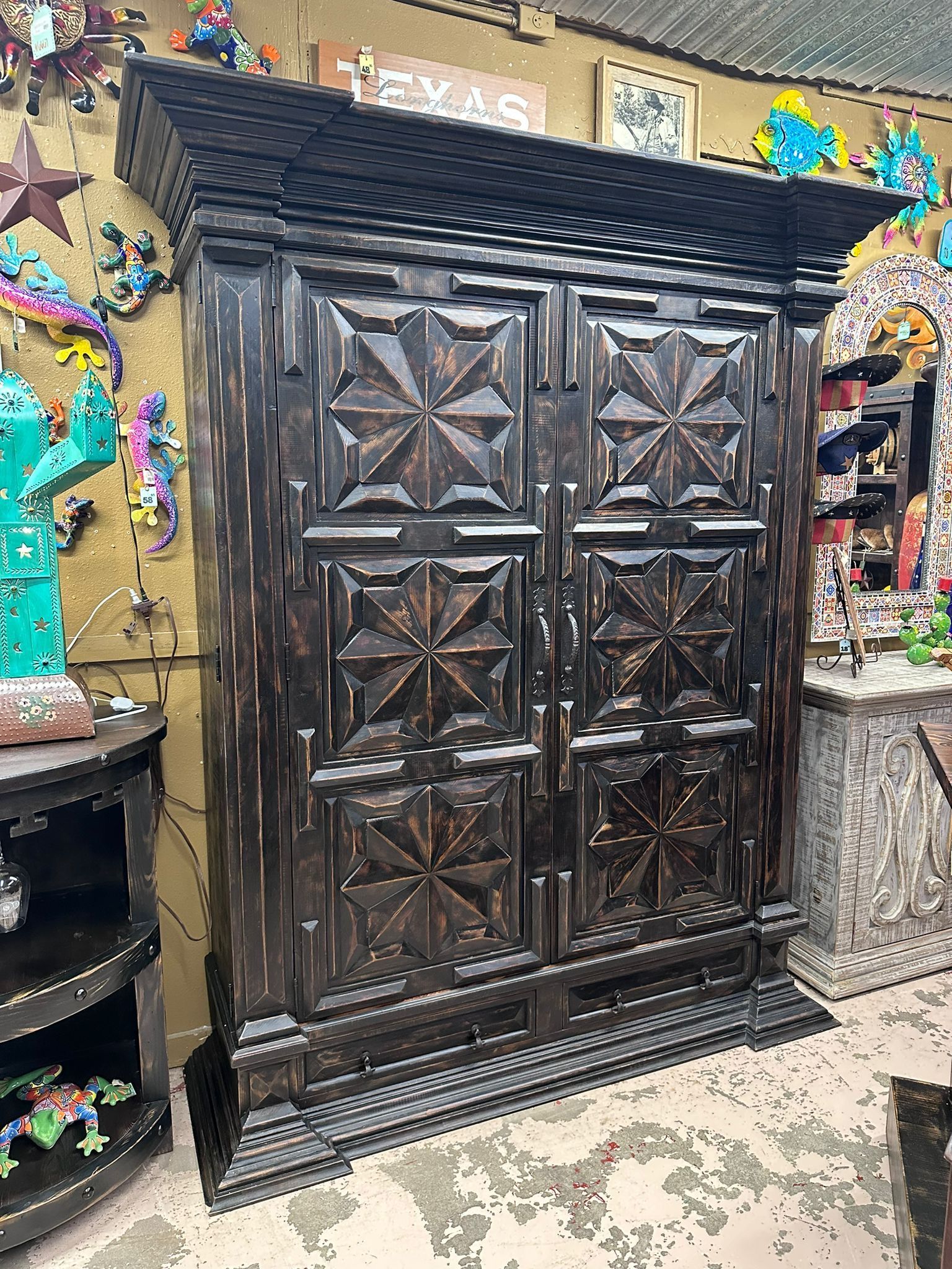 Dark, carved wooden armoire with starburst designs on the doors, set in a cluttered, colorful shop.