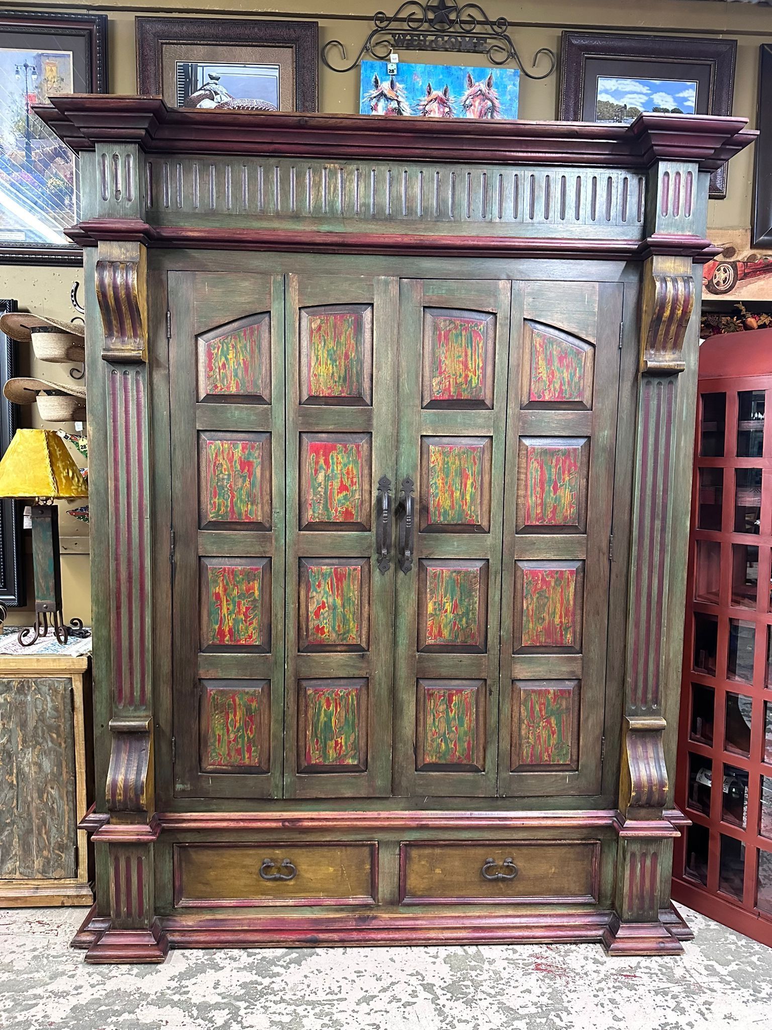 An ornate wooden armoire with green and red paint, two doors, two drawers, and decorative columns.