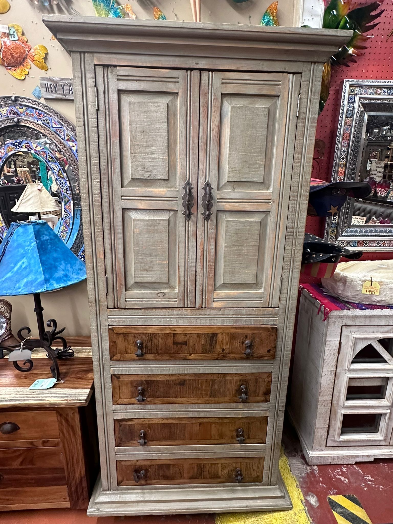 Wooden cabinet with two doors above three drawers, painted in shades of gray and brown, displayed in a shop.