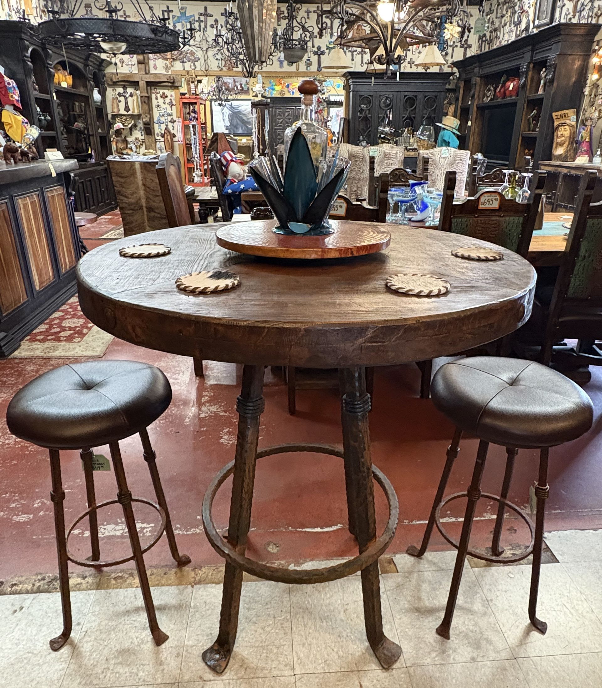 Rustic bar table with two stools in a shop. The dark wood table has decorative coasters and a centerpiece.