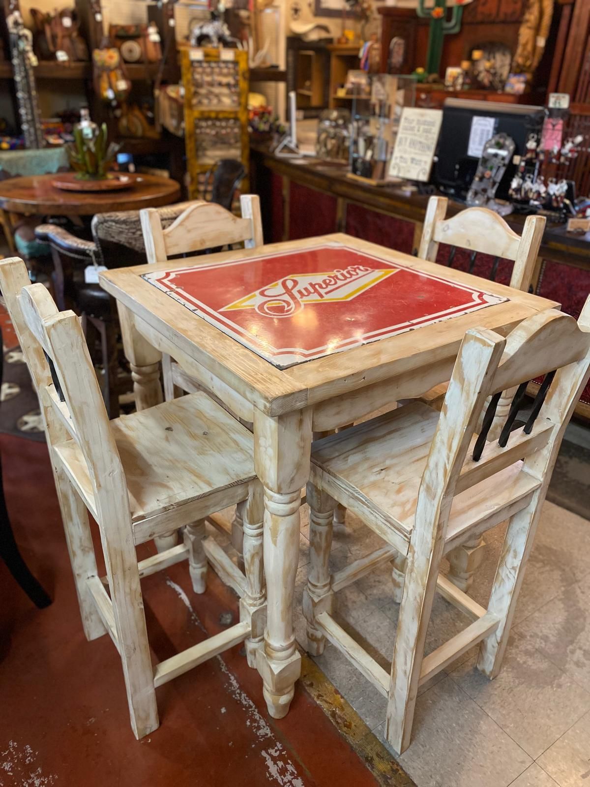 A square, off-white bar table with four matching chairs. The table's top features a red background with 