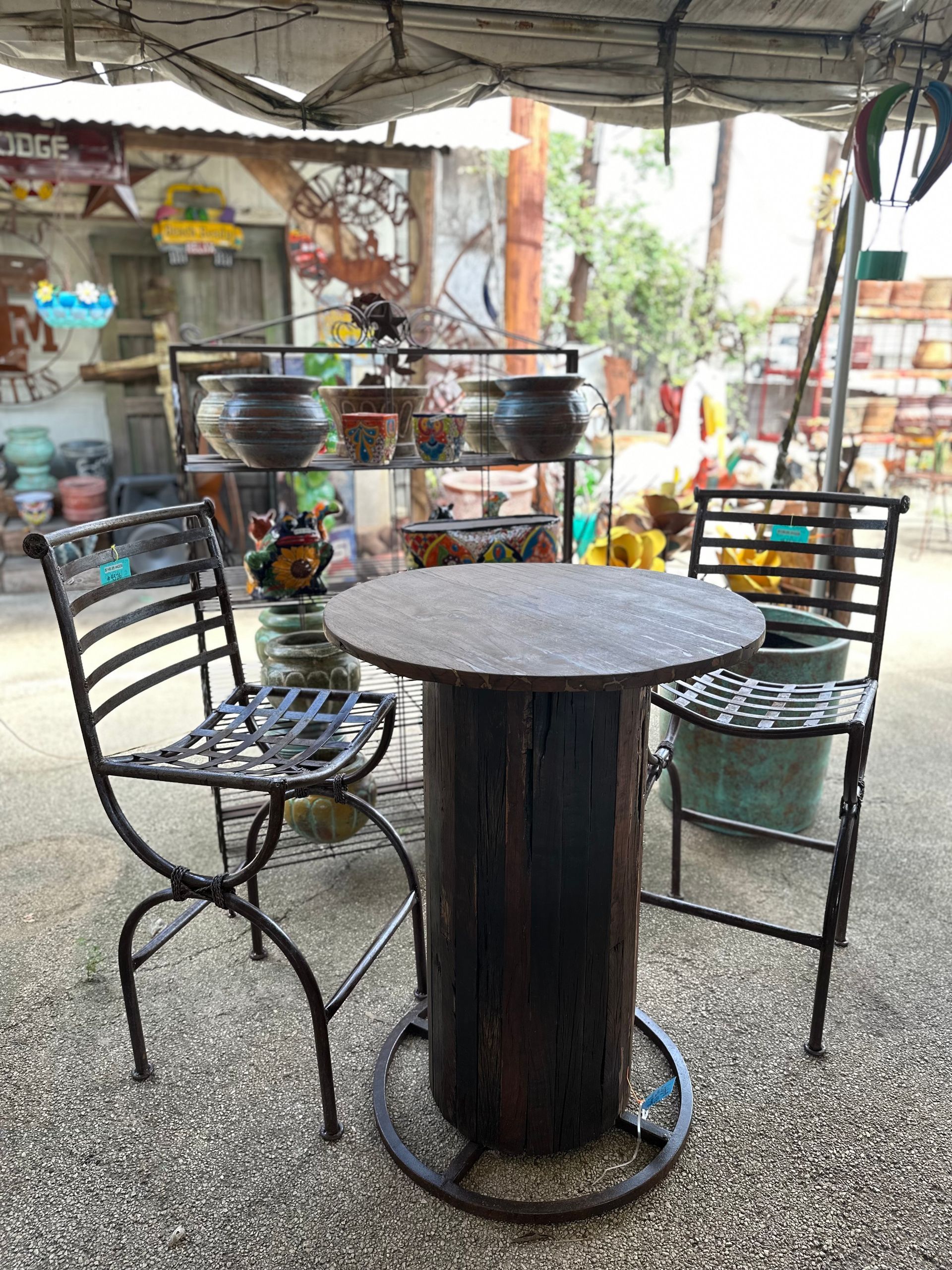 A rustic patio set with two metal chairs and a table made from a wooden spool. The setting is an outdoor shop.