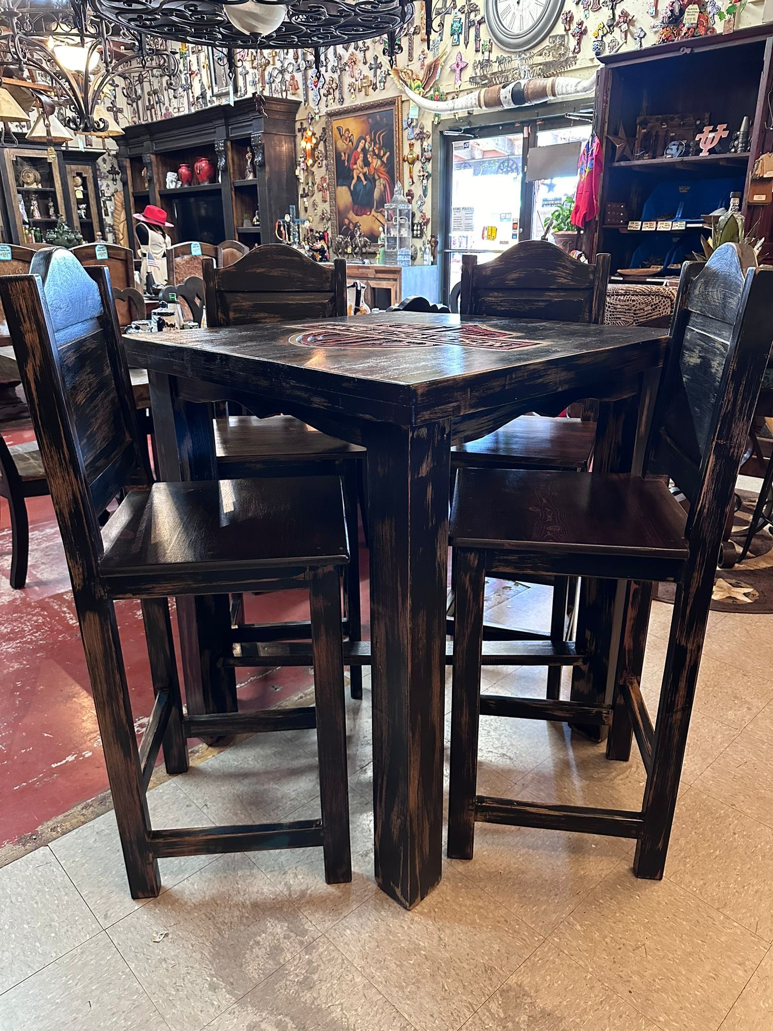 A square, dark wooden bar table with four matching chairs, set inside a shop filled with various items.