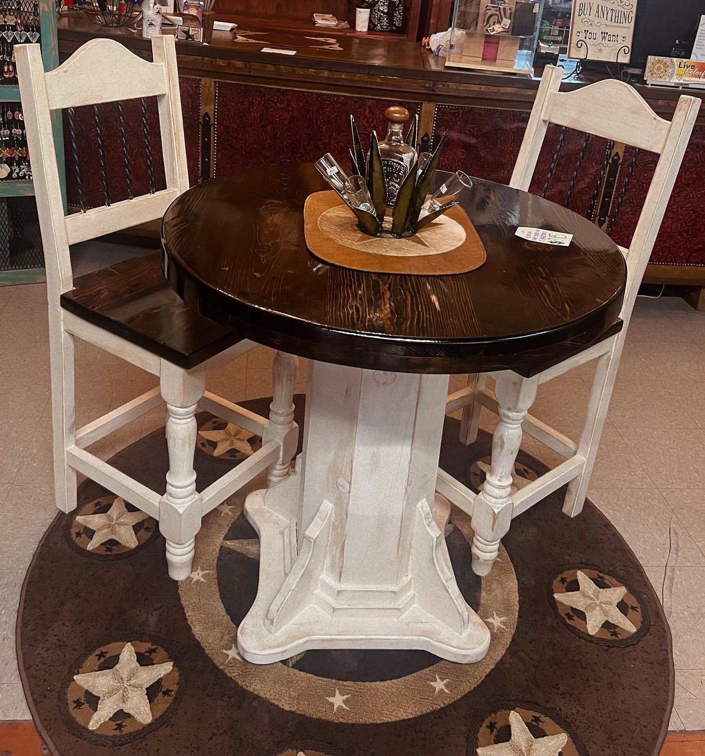 A round, dark wood table with white pedestal base and two white chairs, set on a star-patterned rug.