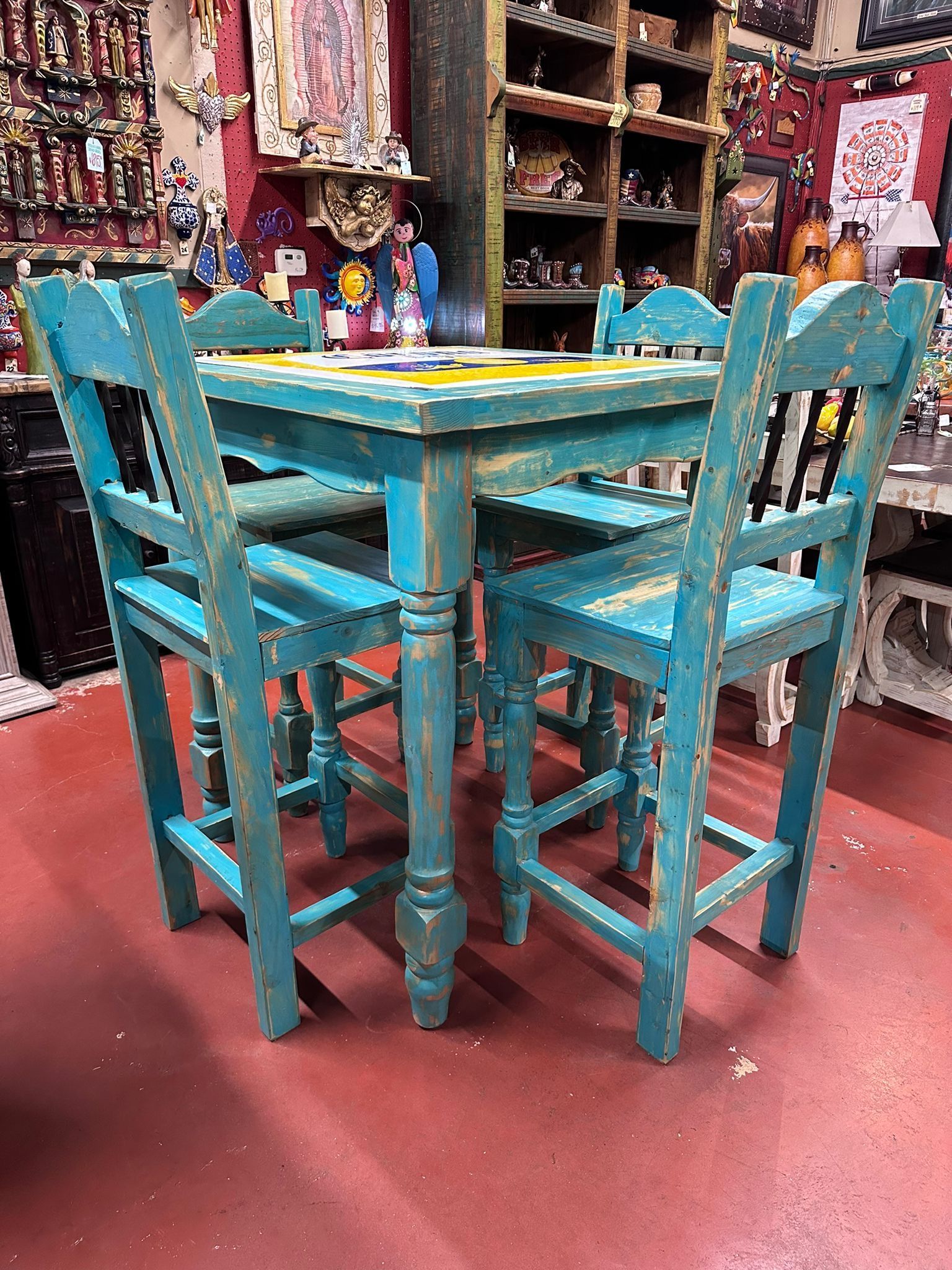 Turquoise-painted wooden table and four chairs with distressed finish, set on red floor in a shop with merchandise on shelves.
