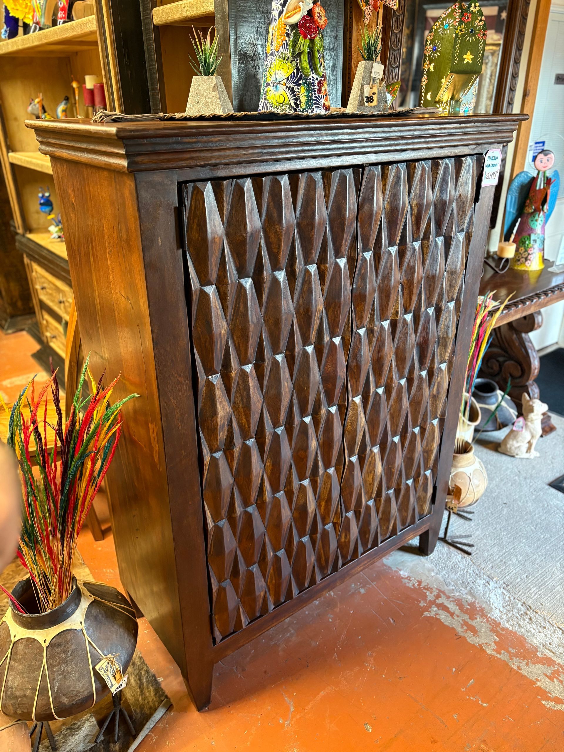 Dark wooden cabinet with textured diamond pattern on the door, set on a red-tiled floor in a shop.