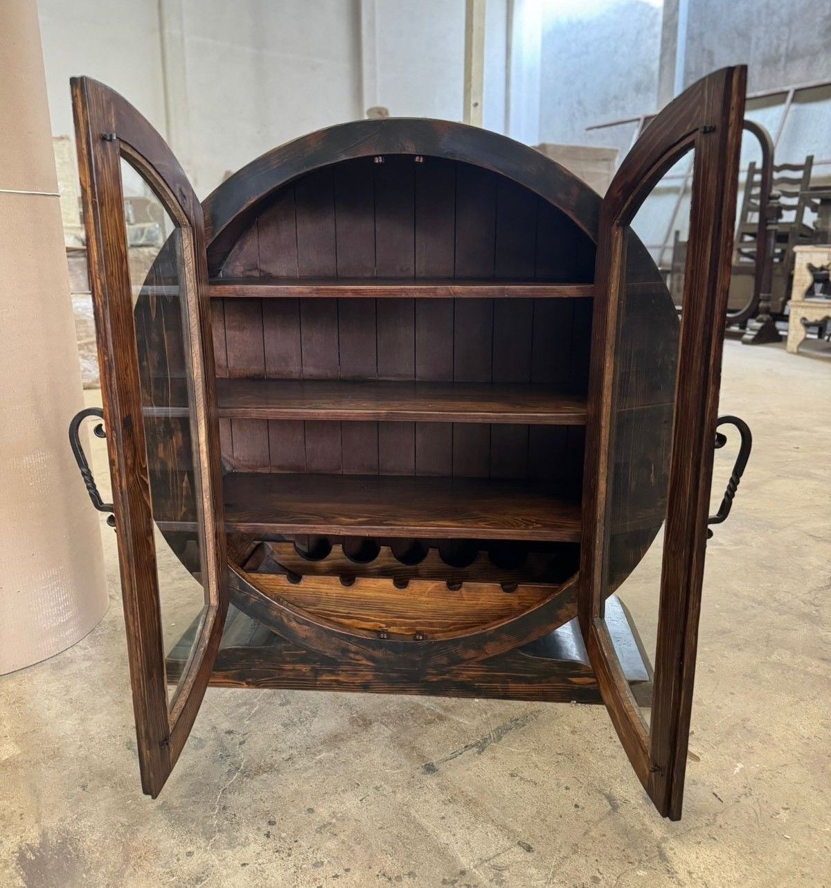 A wooden wine cabinet made from a barrel with glass doors. It has shelves and a wine rack inside.