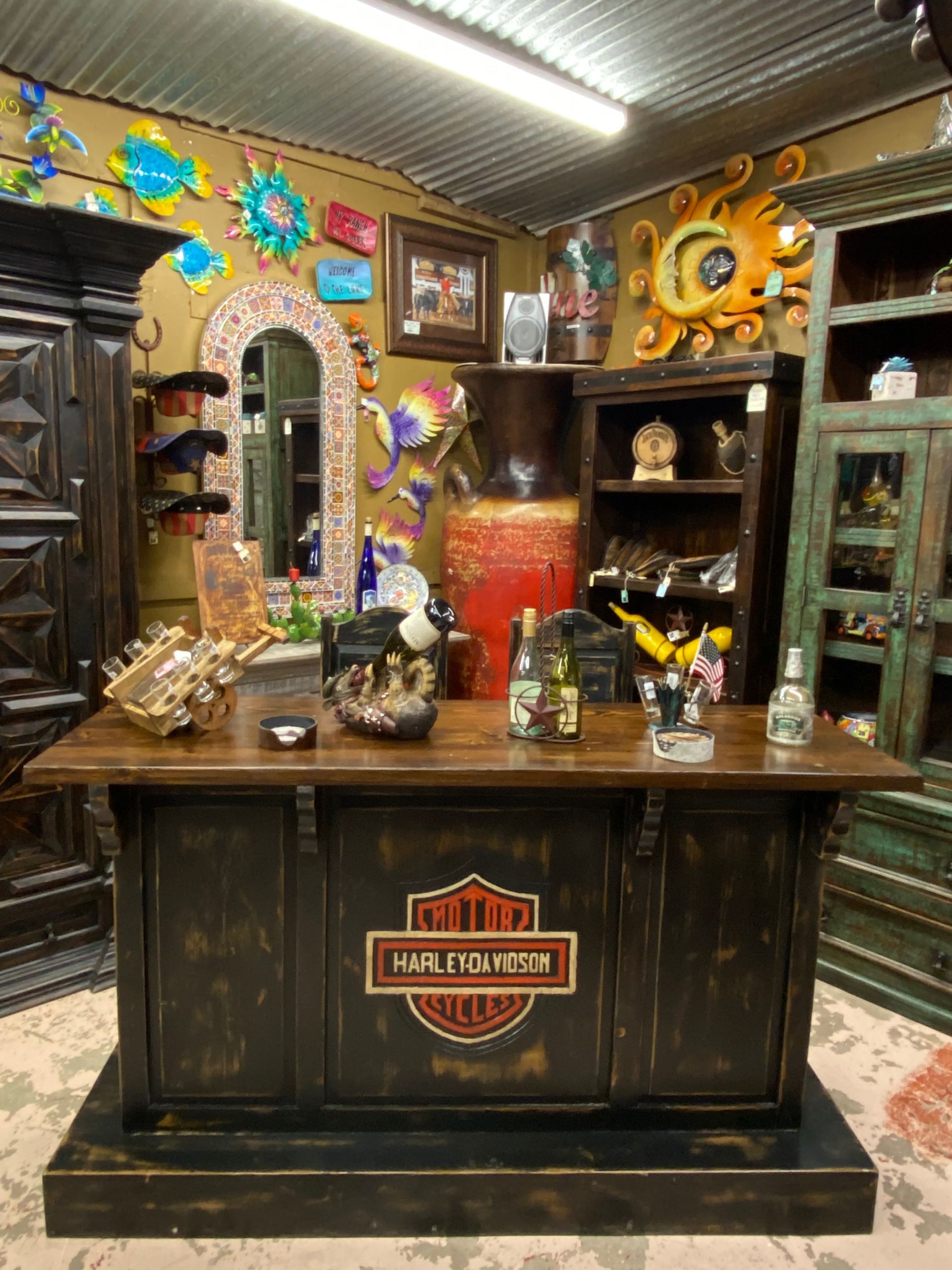 A rustic bar with a Harley Davidson logo on the front is displayed in a shop filled with Southwest-style decor.