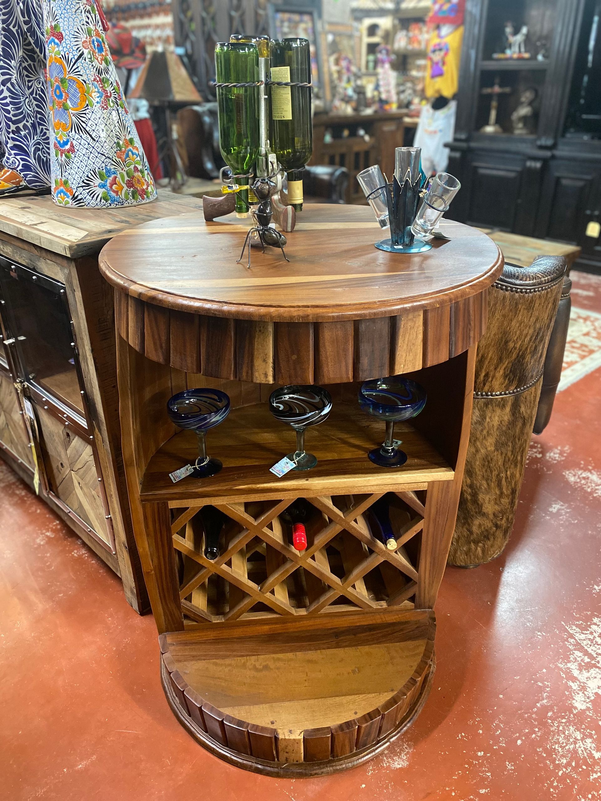 Wooden barrel-shaped wine bar with a round top, wine glass storage, and bottle holders. It's in a store with a reddish-brown floor.