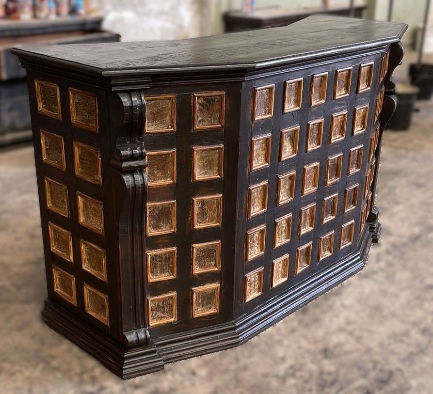 Dark wood bar with gold-toned square inlays. The bar has an ornate design and sits in a blurred indoor setting.