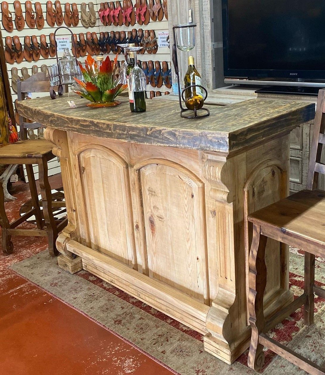 Wooden bar with granite countertop, two wooden stools, bottles, and a decorative floral arrangement.