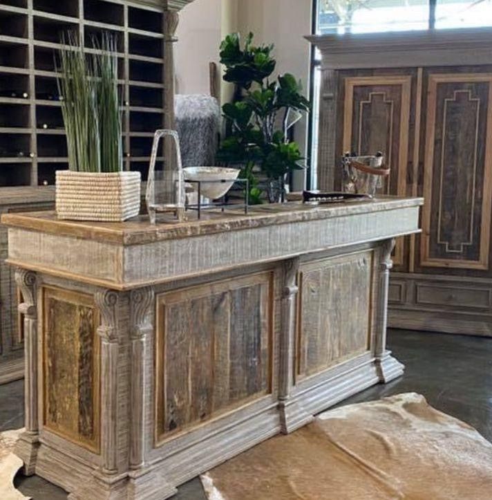 A rustic wooden bar with a marble top, featuring plants and serving items, inside a room with other furniture.
