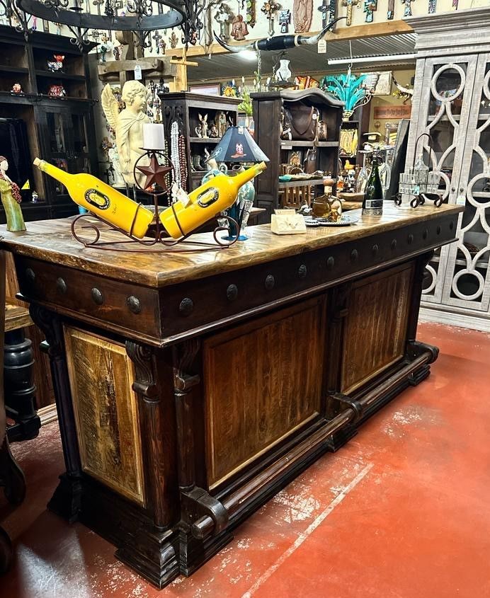 A dark wooden bar with a stone top, displaying wine bottles. The bar is indoors, and various decorative items surround it.