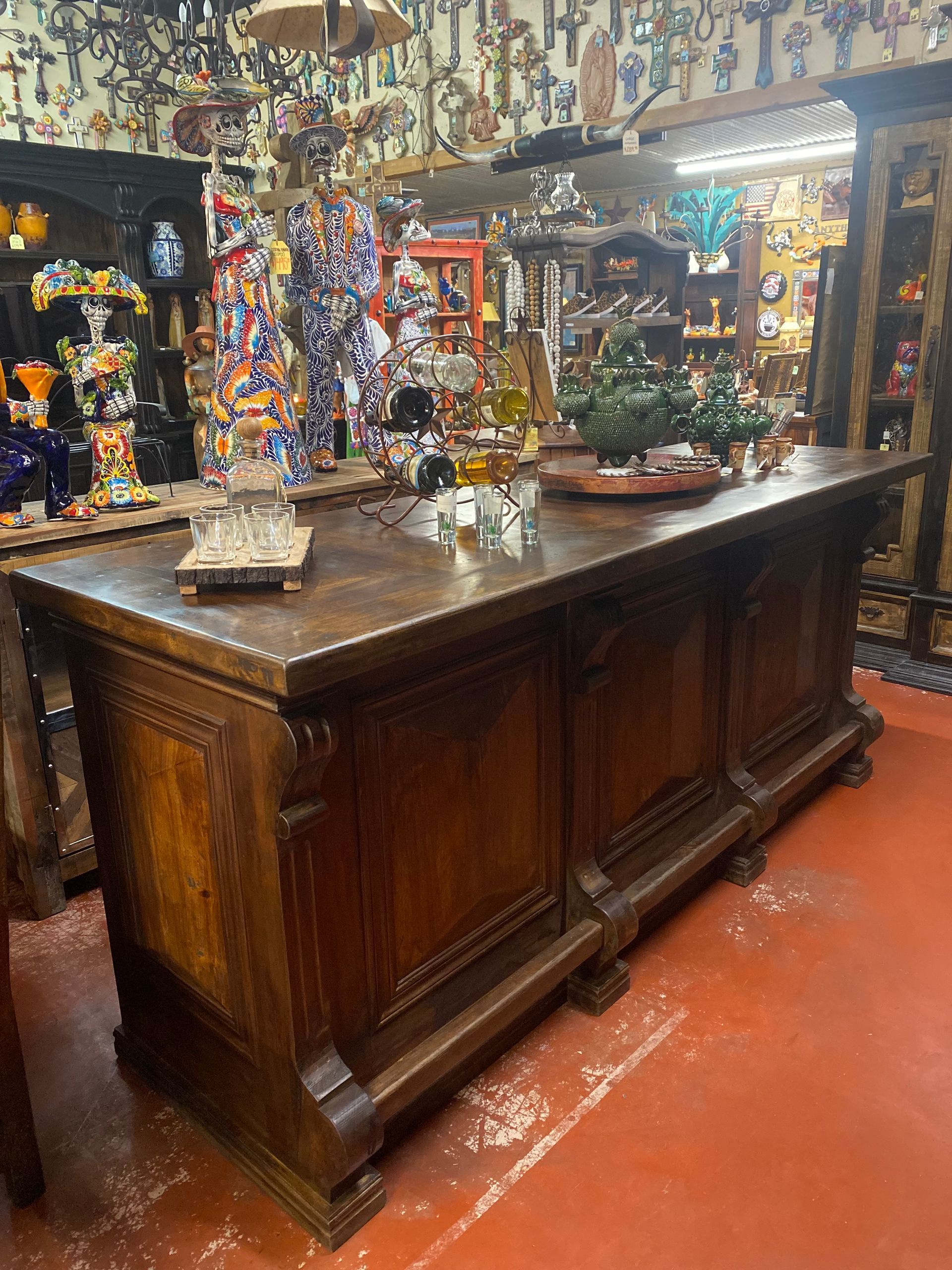 A large, dark wood counter in a store filled with colorful merchandise. The counter has ornate carvings and is cluttered with small objects.
