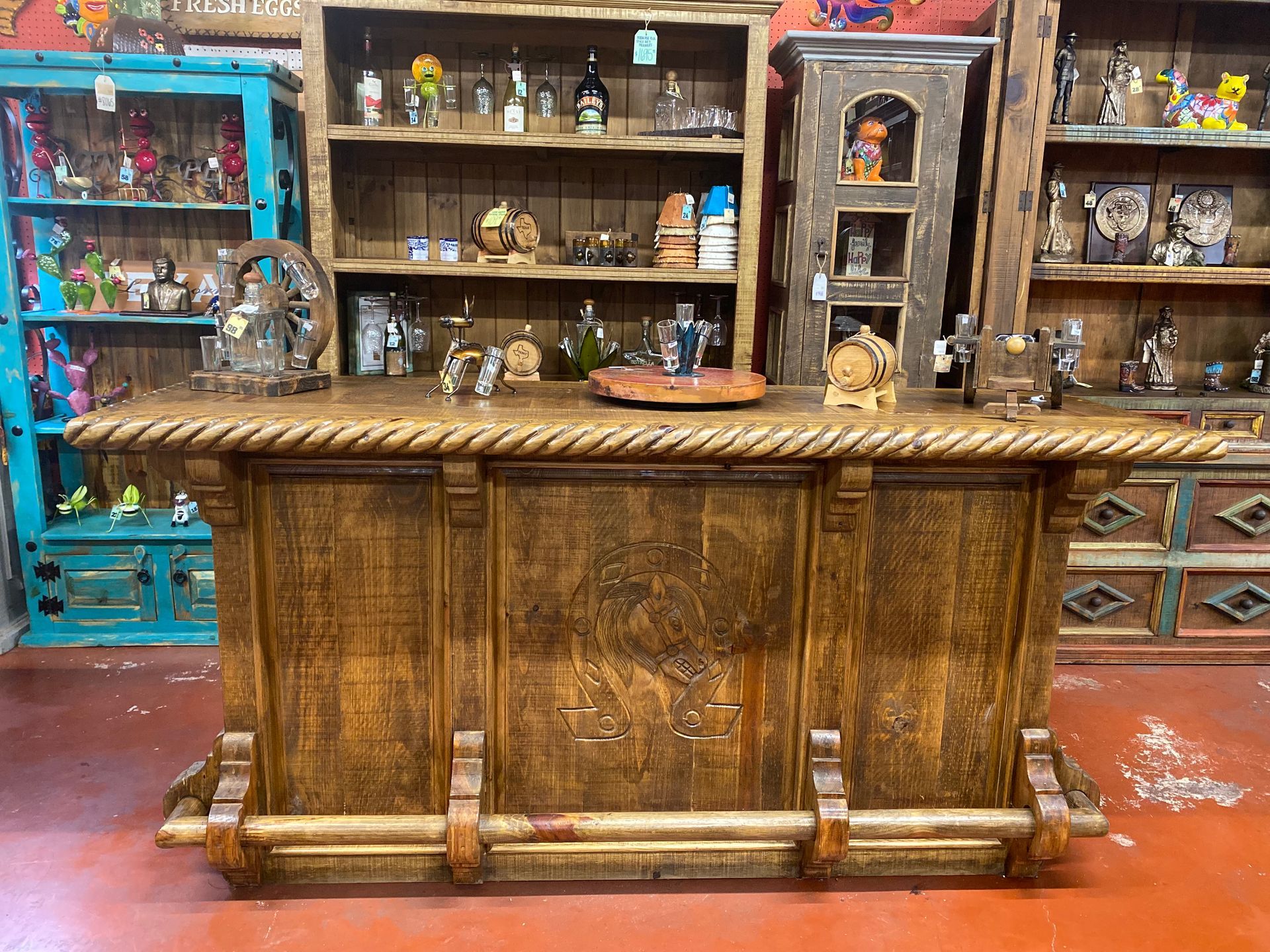 Rustic wooden bar with rope detail and cabinet-style front, set in a shop with shelves of decorative items.