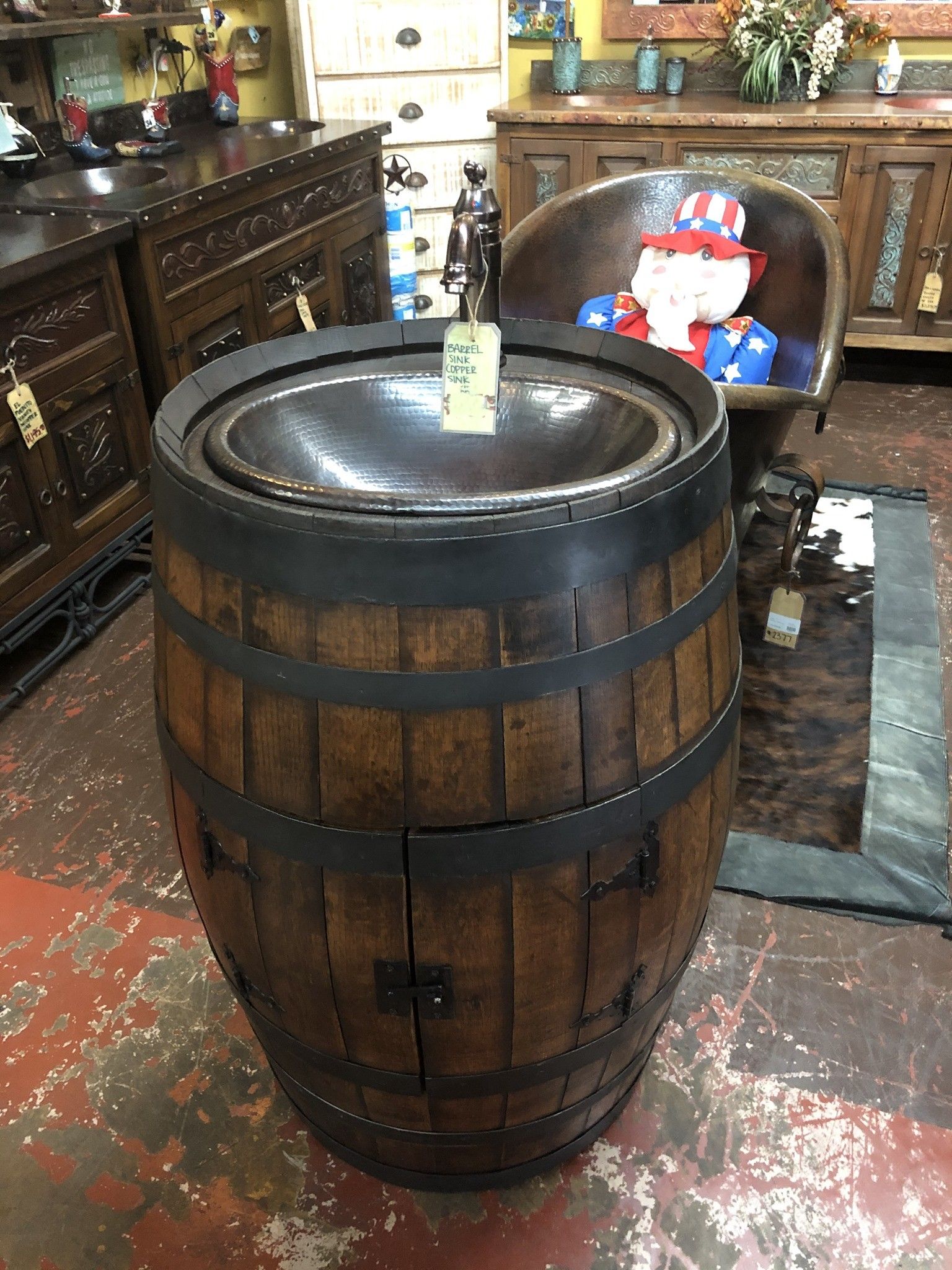 Wooden barrel sink with a dark-colored bowl. It has metal bands and a small cabinet door.