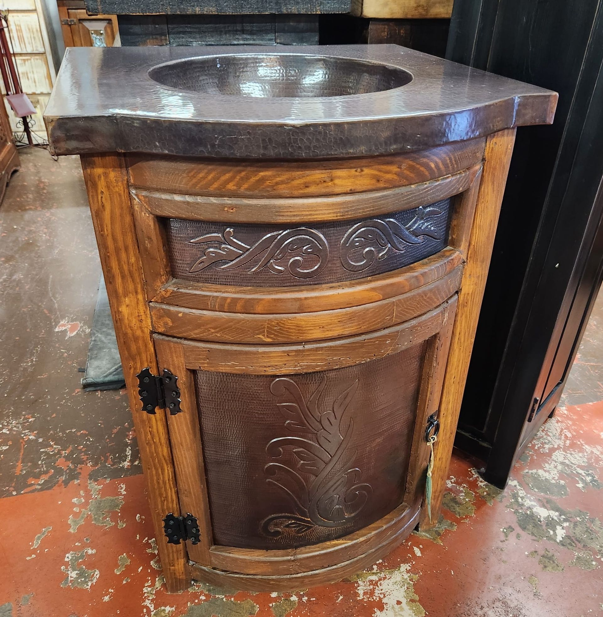 Bathroom vanity with a dark countertop and a bowl sink, over a wooden cabinet with decorative metal panels.