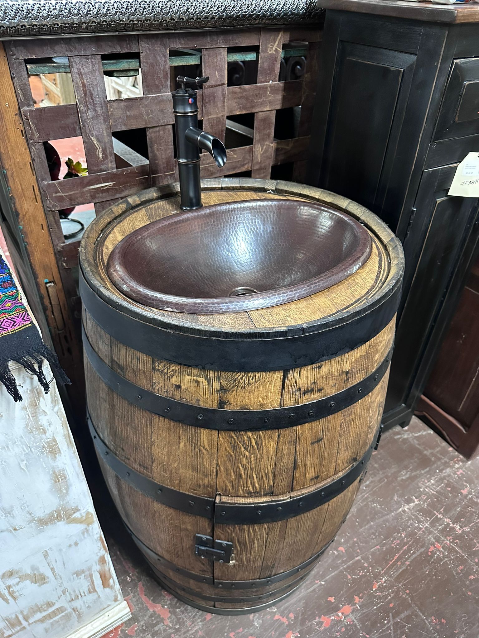 A wooden barrel repurposed as a sink with a dark basin and faucet. The barrel has metal bands and sits indoors.