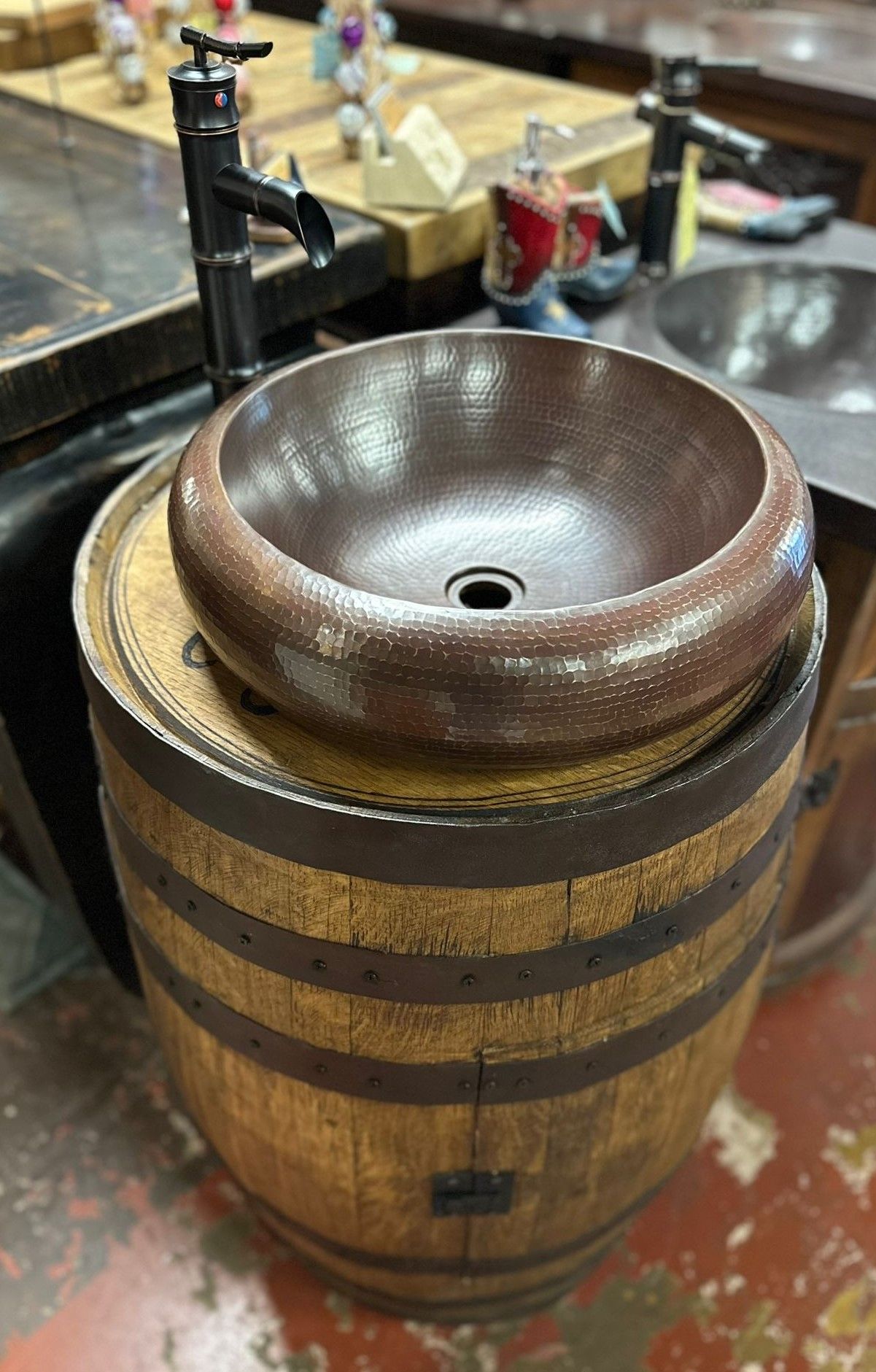 A copper sink rests on a wooden barrel with a black faucet in a showroom.