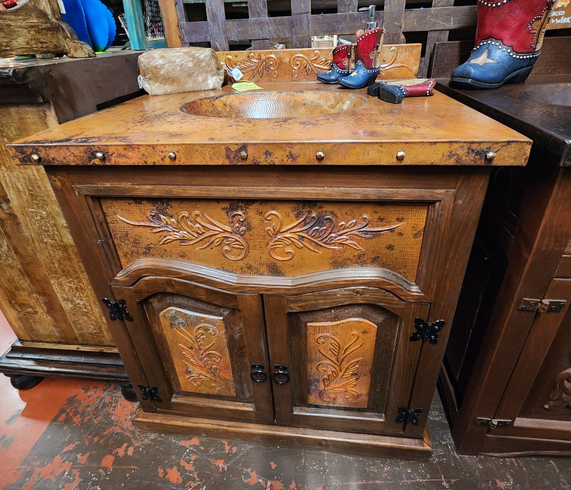 Rustic bathroom vanity with copper countertop and decorative panels. Features a single sink, two doors, and decorative hardware.