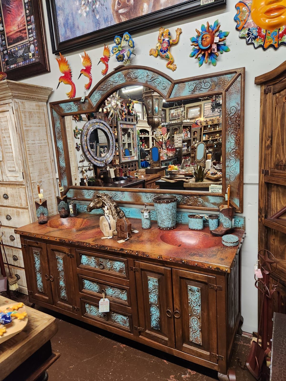 Wooden vanity with turquoise accents and a large mirror, featuring two red sinks and decorative items in a shop.