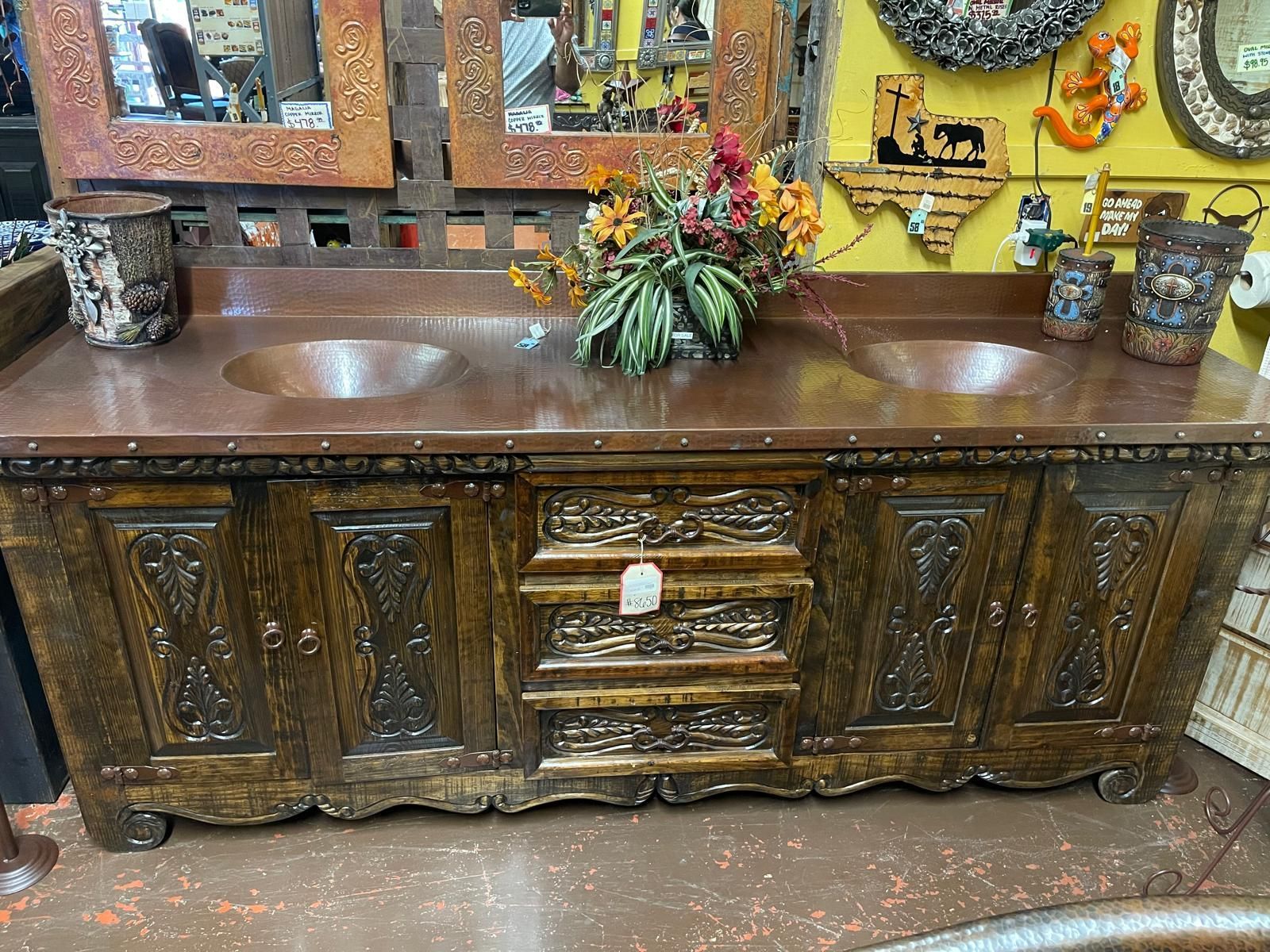 Wooden double bathroom vanity with copper sinks, adorned with carvings and floral arrangements.