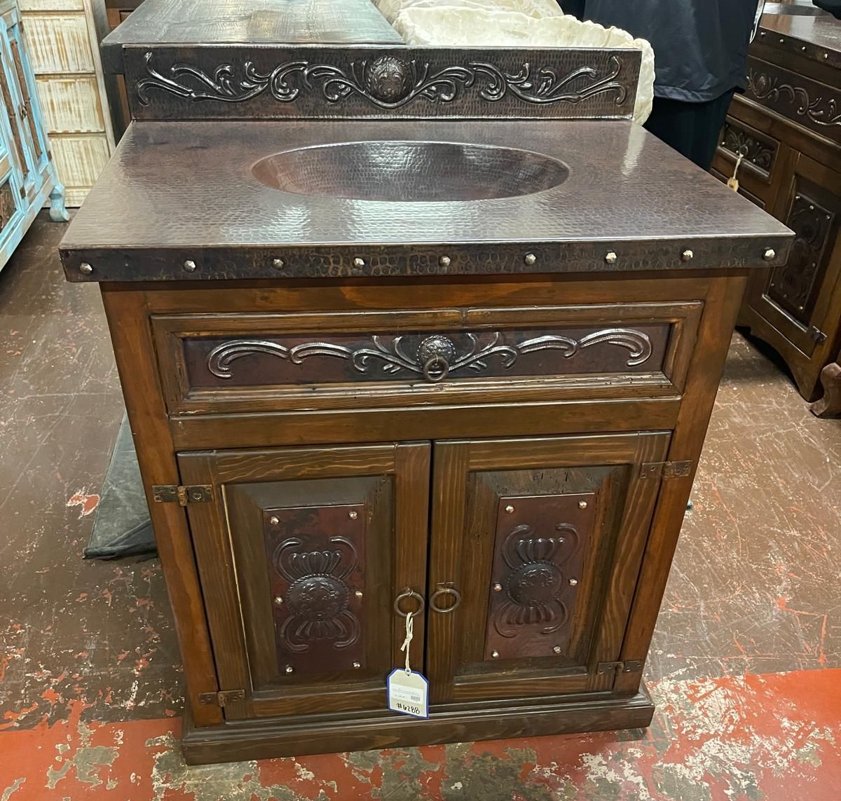 Wooden bathroom vanity with copper-toned countertop and decorative accents. It has a central sink basin and cabinet doors below.