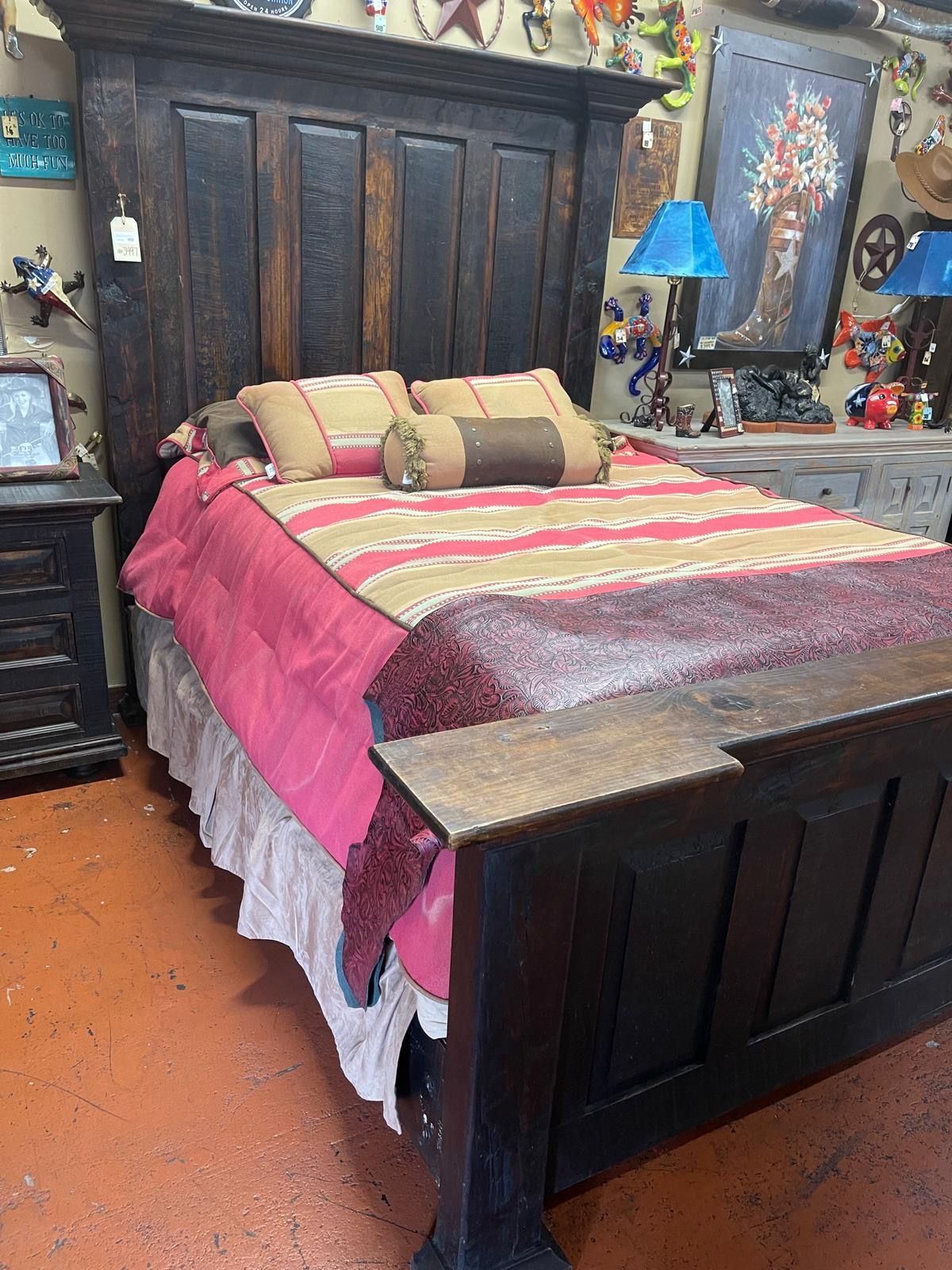 Dark wooden bed with a tall headboard, made up with a pink and striped comforter.