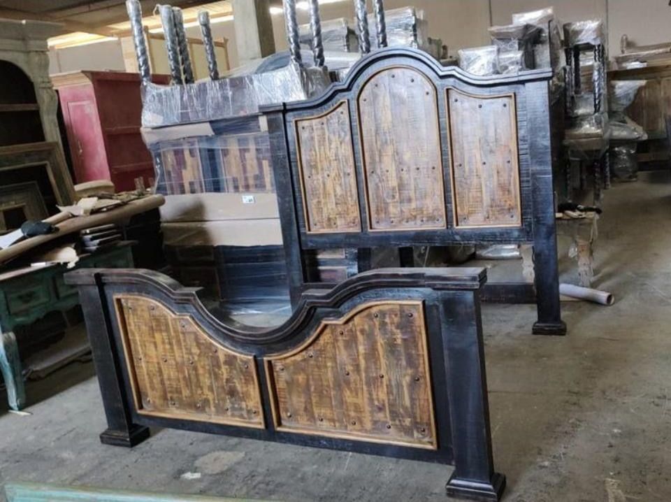 Black and brown wooden bed frame and headboard in a warehouse setting. The bed has a rustic design with vertical wooden panels.