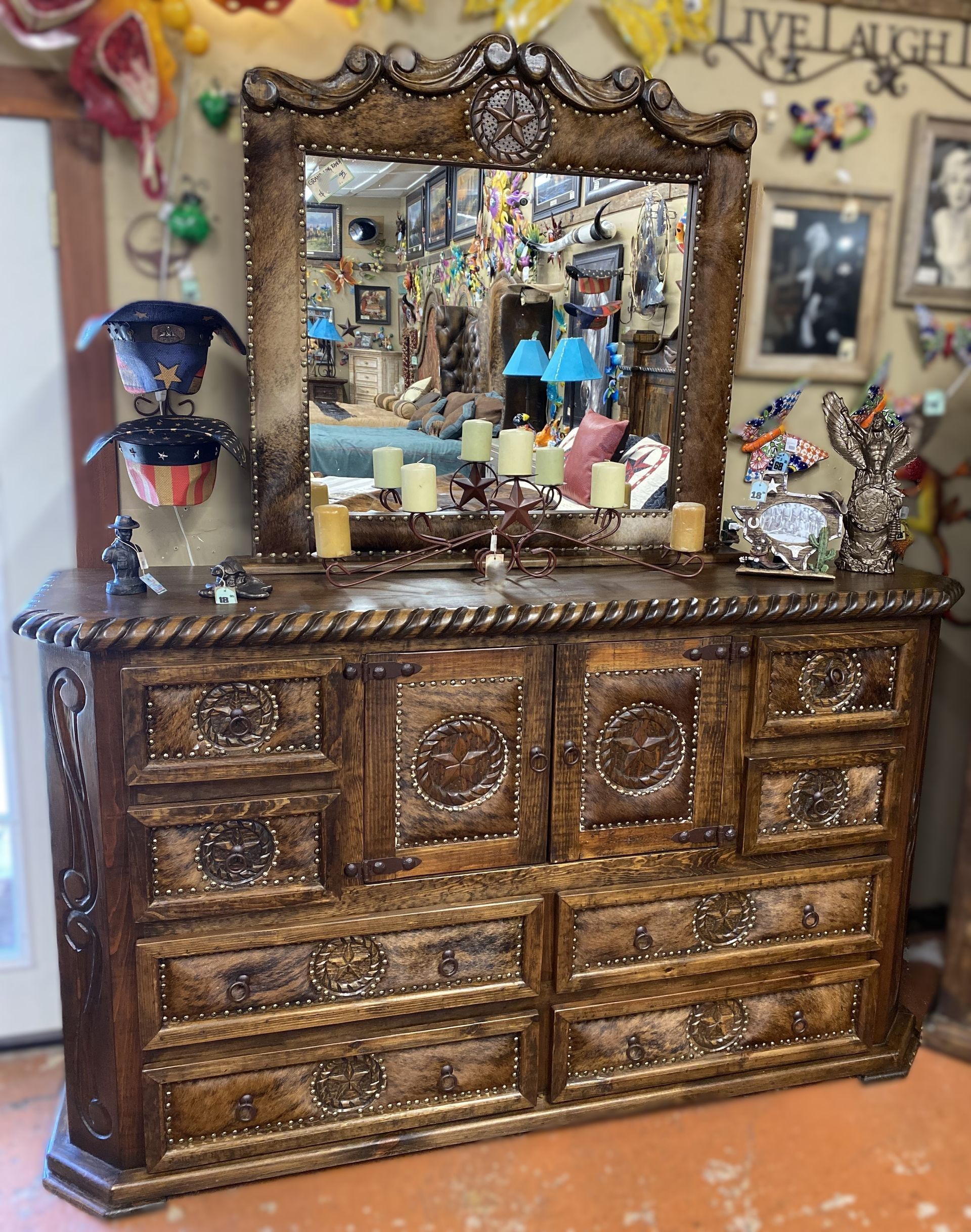 Ornate wooden dresser with a mirror, decorated with candles and items in a room filled with various objects.