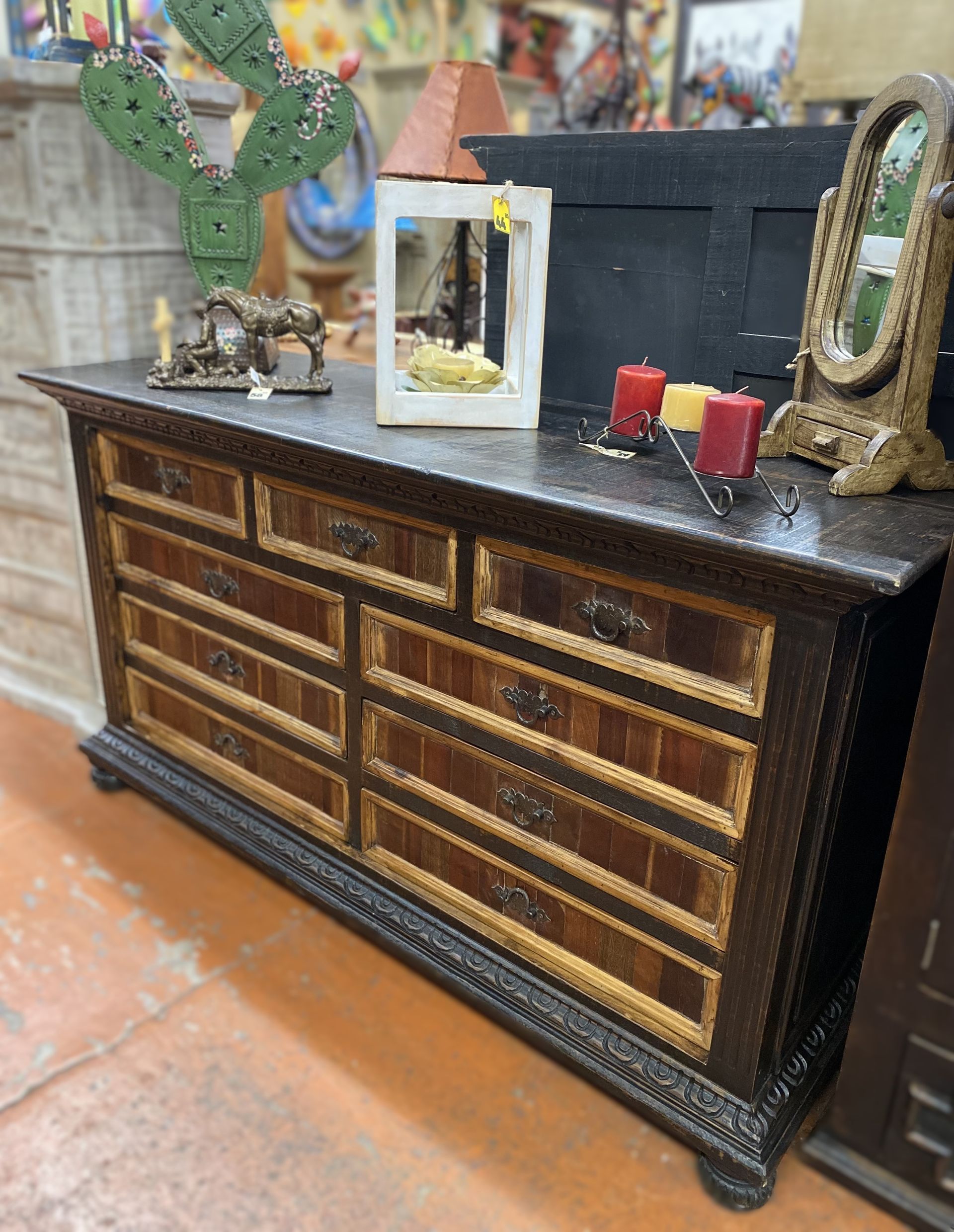 A wooden dresser with several drawers, decorated in a southwestern style, with decorative items on top.