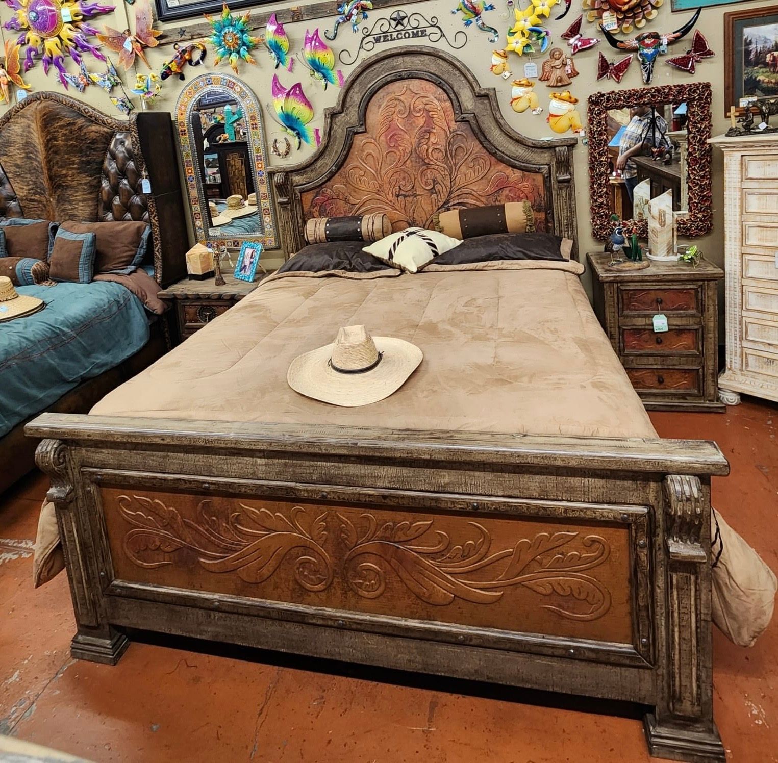 Wooden bed with ornate headboard, nightstands, and a cowboy hat on the bedspread in a brightly decorated shop.