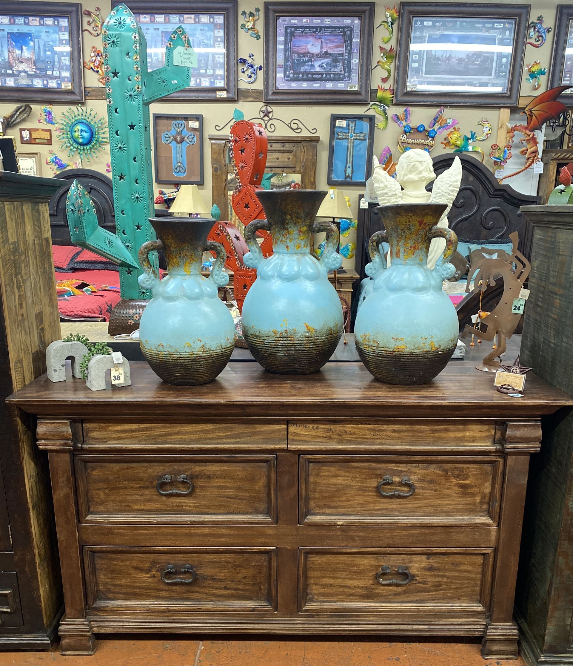 Three turquoise vases on a wooden dresser, decorated in a southwestern style shop. Cactus art and other decor in the background.