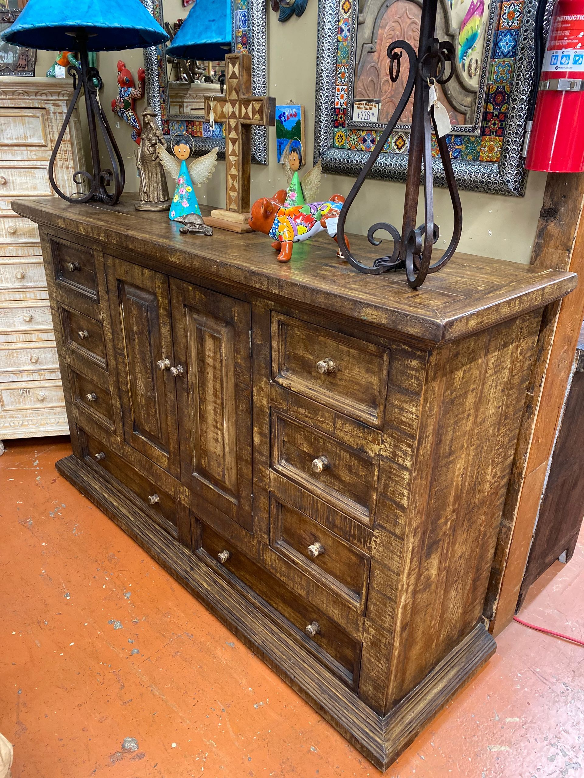 A large, rustic wooden dresser with drawers and cabinet doors in a room filled with decorative items.
